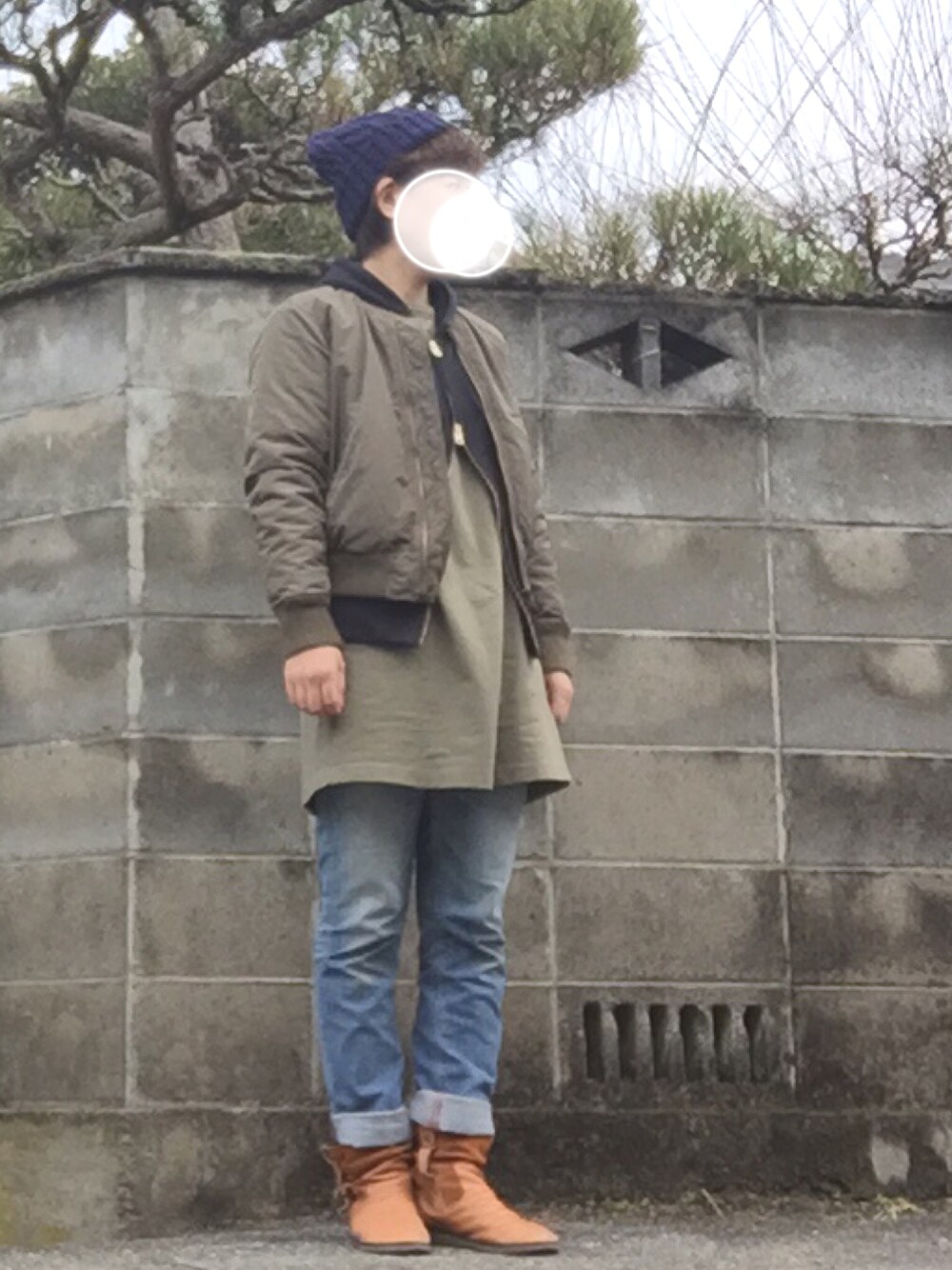 グリーン系のワンピース、ブルー系のデニムパンツ、ベージュ系のブーツを着用したレディースの冬コーディネートの1枚目の写真