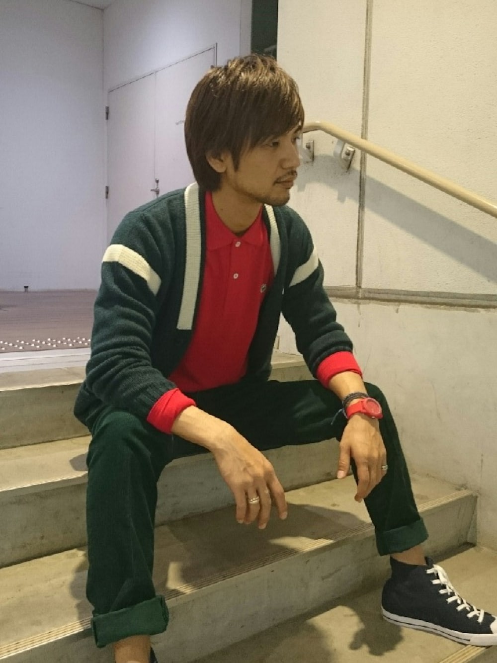 ブルー系のスニーカー、グリーン系のカーディガン/ボレロ、レッド系のポロシャツを着用したメンズの秋コーディネートの1枚目の写真