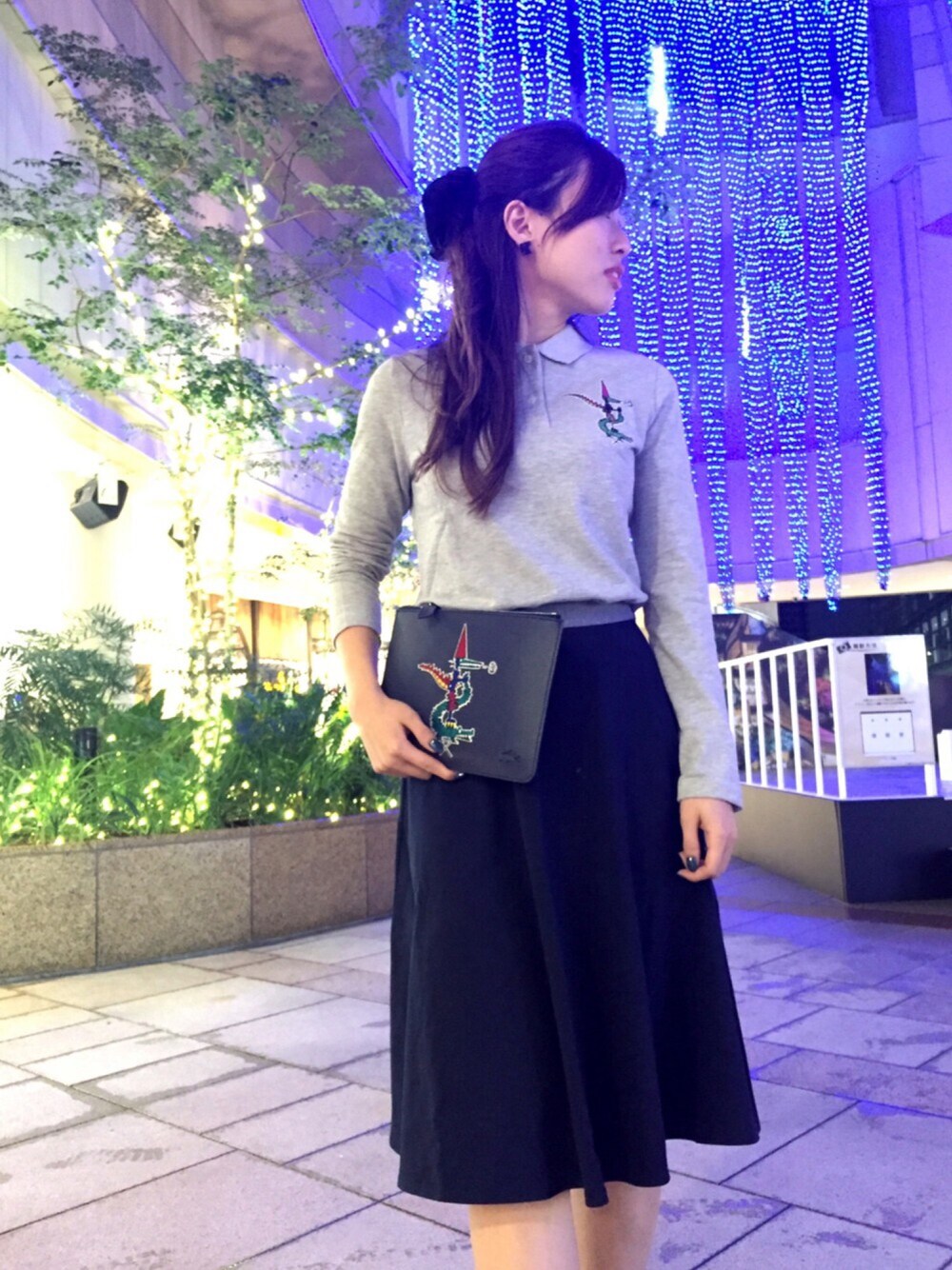 グレー系のポロシャツ、ブラック系のクラッチバッグ、ブルー系のスカートを着用したレディースの秋コーディネートの1枚目の写真