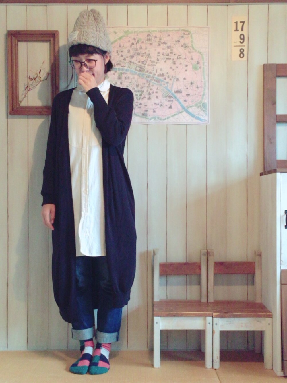 ブラック系のカーディガン/ボレロ、ホワイト系のシャツワンピース、ブルー系のデニムパンツを着用したレディースの秋コーディネートの1枚目の写真