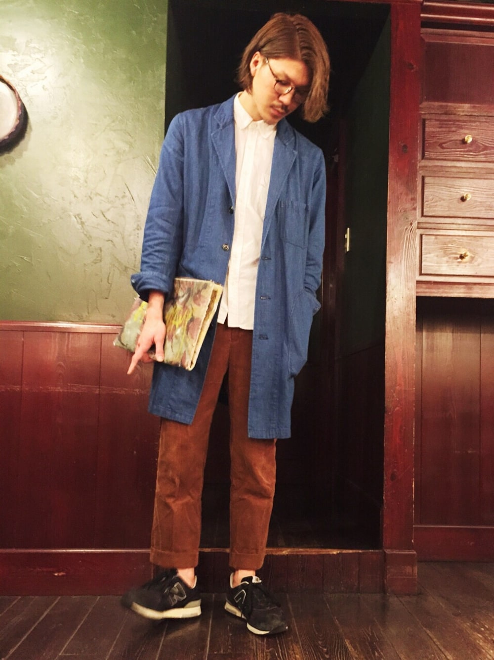 ブルー系のチェスターコート、ブラウン系のその他パンツ、グリーン系のクラッチバッグを着用したメンズの冬コーディネートの1枚目の写真