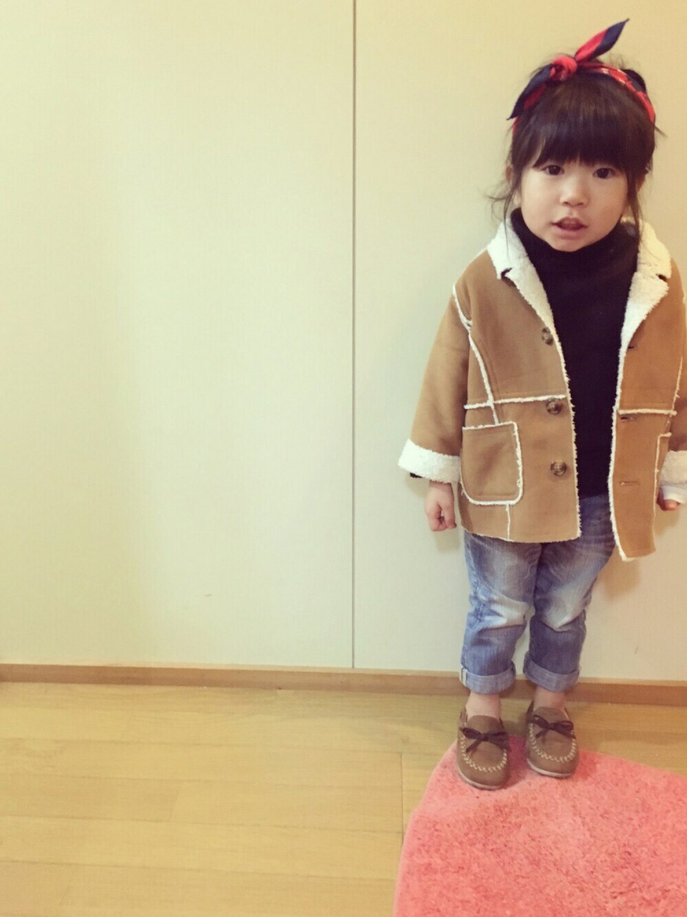 ブラウン系のムートンコート、ブラック系のニット/セーター、ブルー系のデニムパンツを着用したキッズの春コーディネートの1枚目の写真