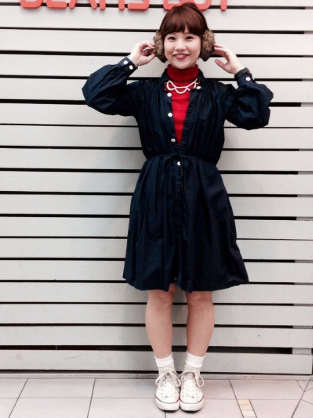 レッド系のニット/セーター、ベージュ系のイヤーマフを着用したレディースの秋コーディネートの1枚目の写真