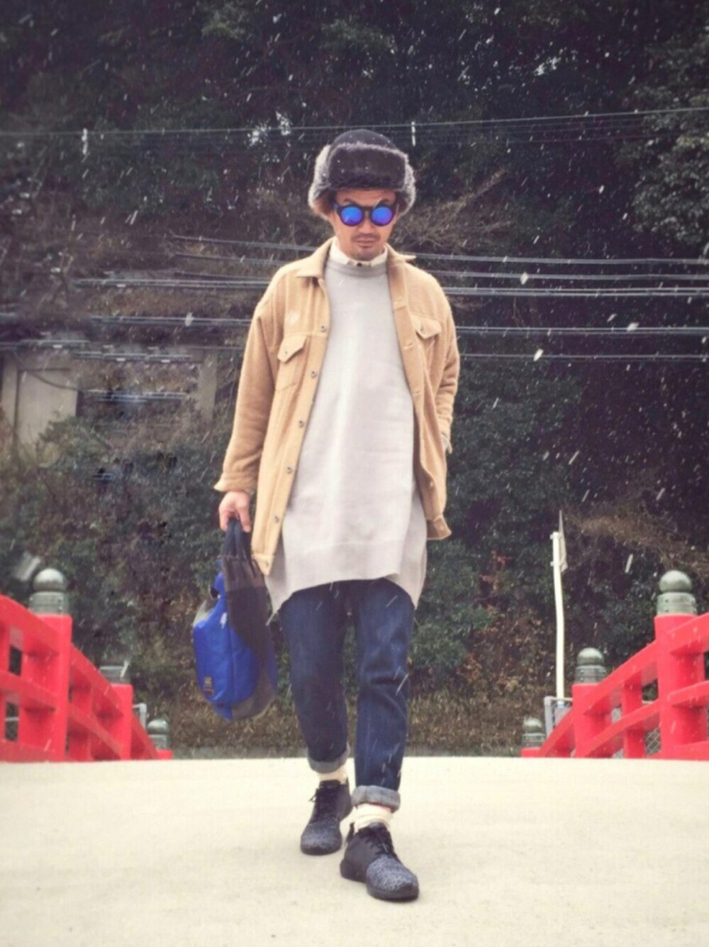 グレー系のニット/セーター、ブルー系のショルダーバッグ、ブラック系のスニーカーを着用したメンズの冬コーディネートの1枚目の写真