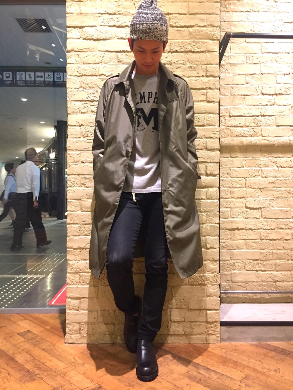 グリーン系のステンカラーコート、グレー系のニット/セーター、ブラック系のデニムパンツを着用したメンズの秋コーディネートの1枚目の写真