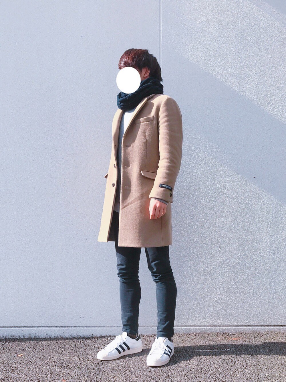 ホワイト系のスニーカー、ブラック系のデニムパンツ、ベージュ系のチェスターコートを着用したメンズの冬コーディネートの1枚目の写真