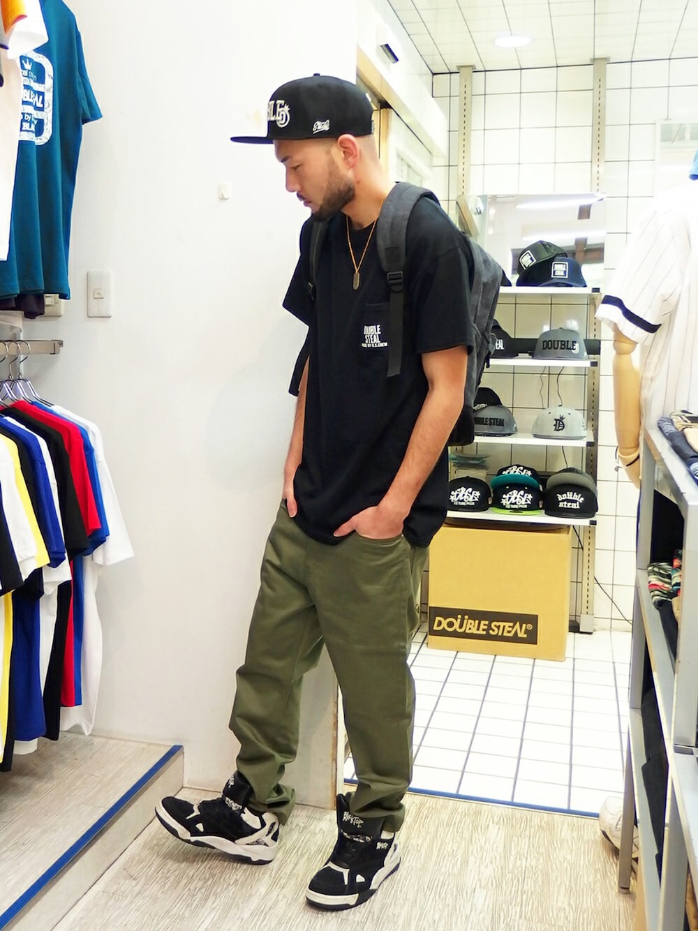ブラック系のTシャツ/カットソー、グリーン系のチノパンツ、ブラック系のバックパック/リュックを着用したメンズの春コーディネートの1枚目の写真