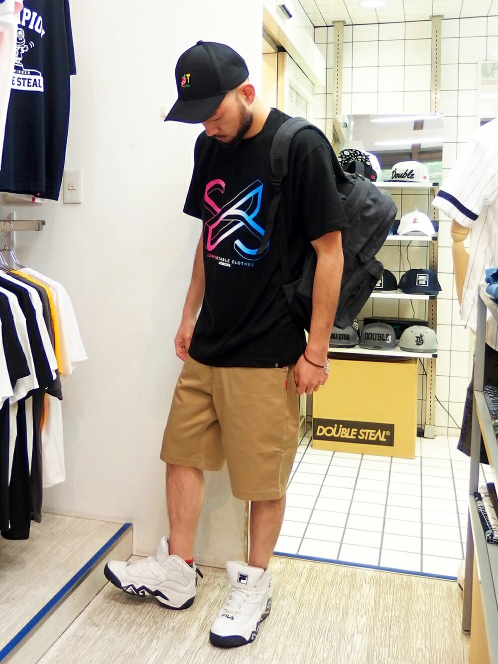 ブラック系のTシャツ/カットソー、ベージュ系のチノパンツ、ブラック系のバックパック/リュックを着用したメンズの春コーディネートの1枚目の写真