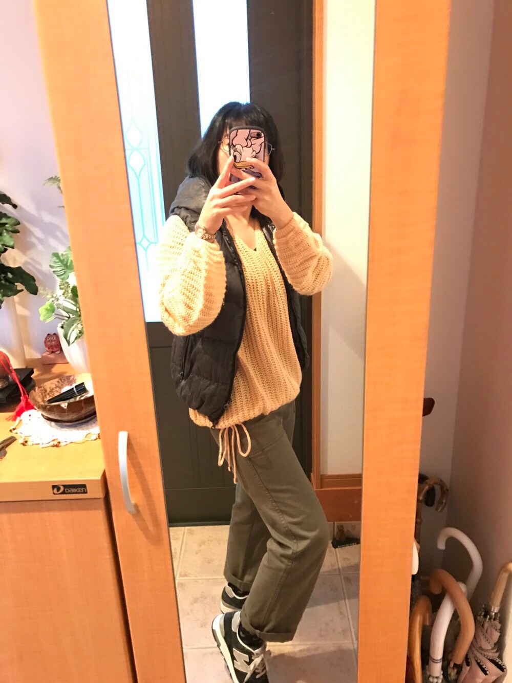 オレンジ系のニット/セーター、グレー系のダウンベスト、グリーン系のその他パンツを着用したレディースの秋コーディネートの1枚目の写真