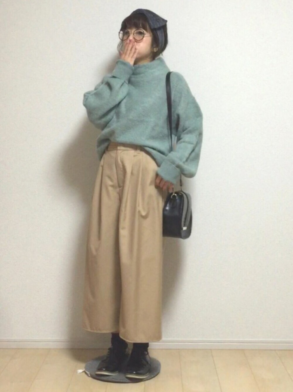 グリーン系のニット/セーター、ベージュ系のパンツ、ブラック系のショルダーバッグを着用したレディースの秋コーディネートの1枚目の写真