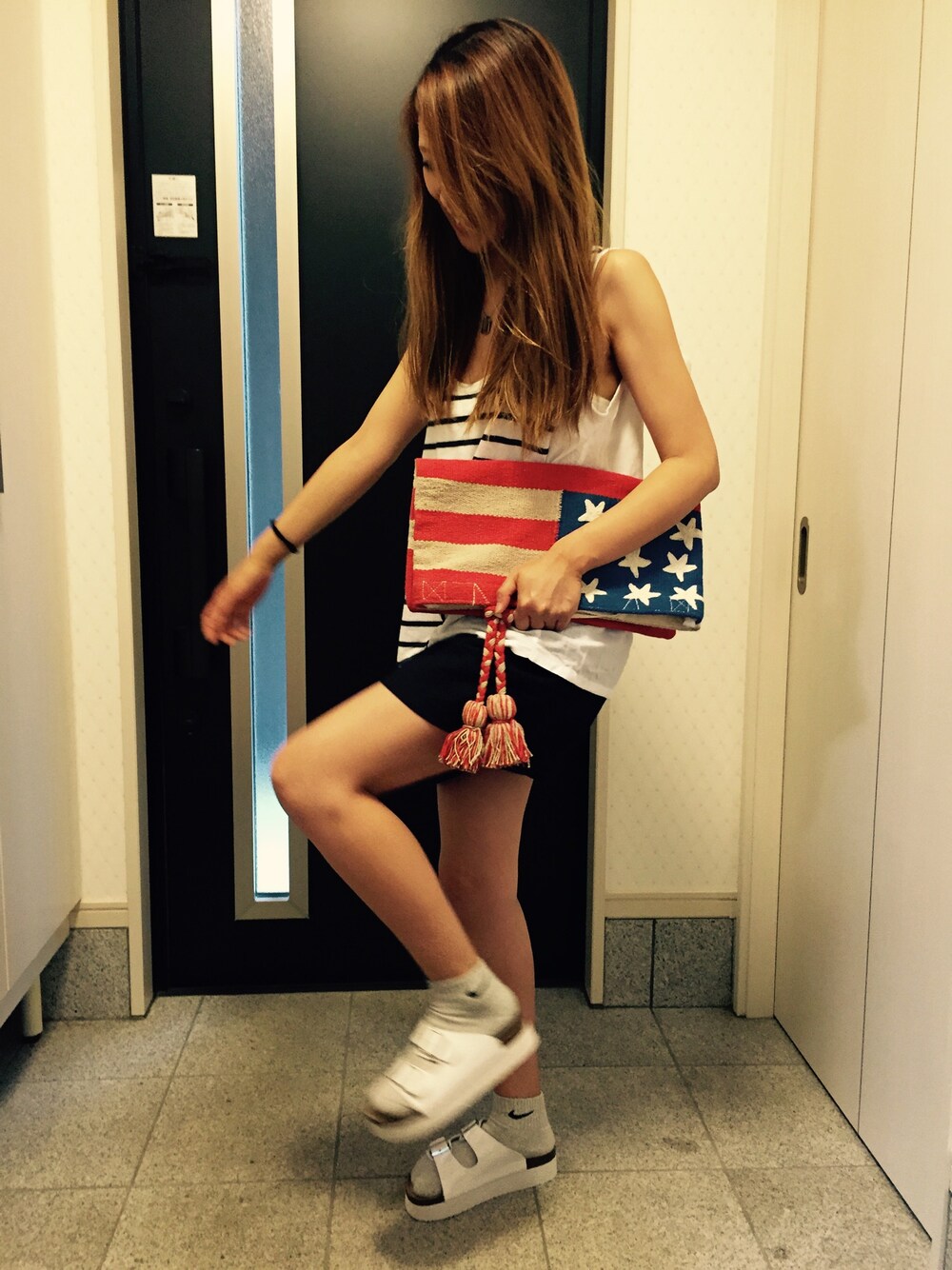 レッド系のクラッチバッグ、ブルー系のパンツ、ホワイト系のトップスを着用したレディースの夏コーディネートの1枚目の写真