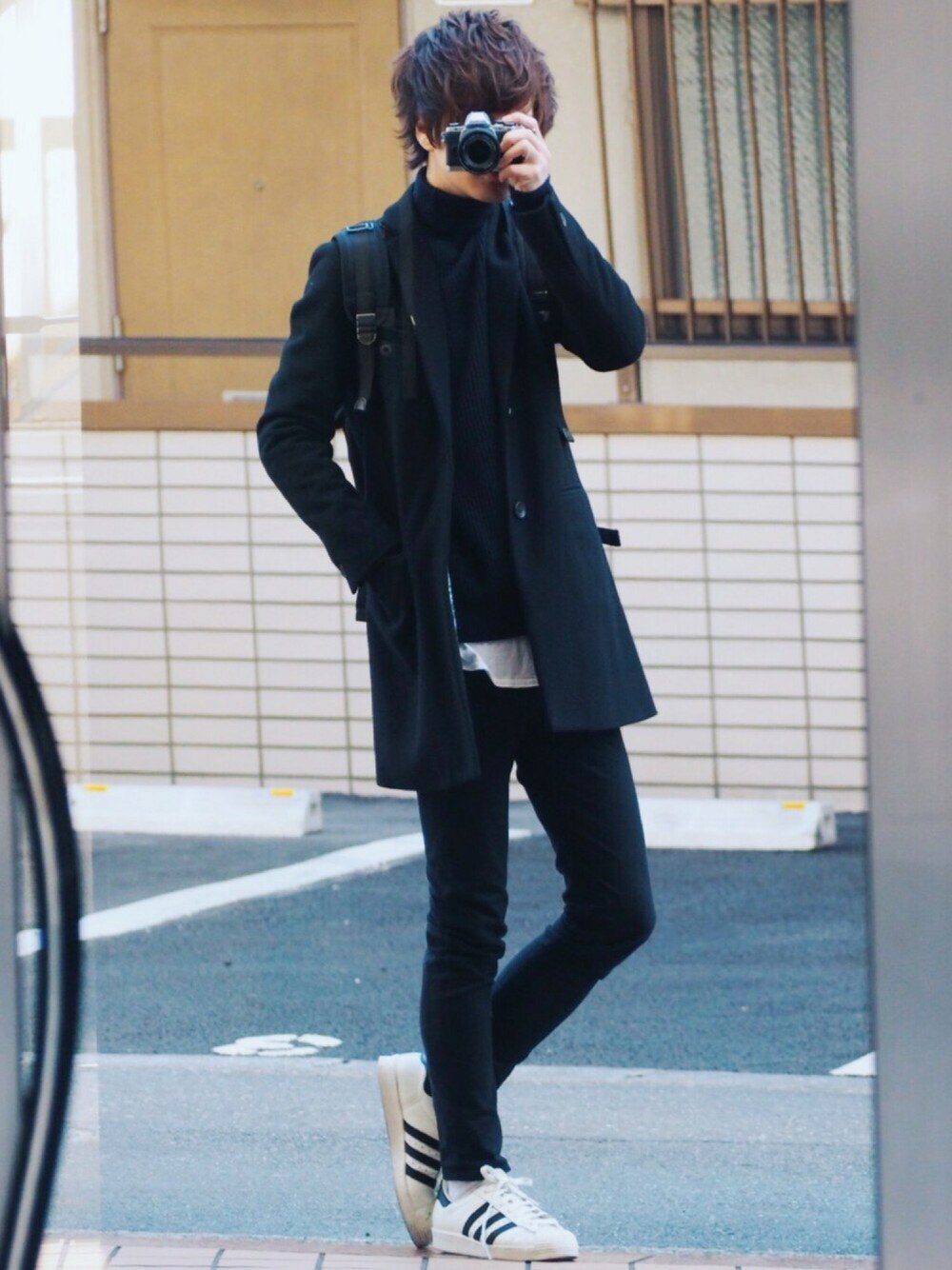 ブラック系のチェスターコート、ブルー系のニット/セーター、ホワイト系のTシャツ/カットソーを着用したメンズの冬コーディネートの1枚目の写真