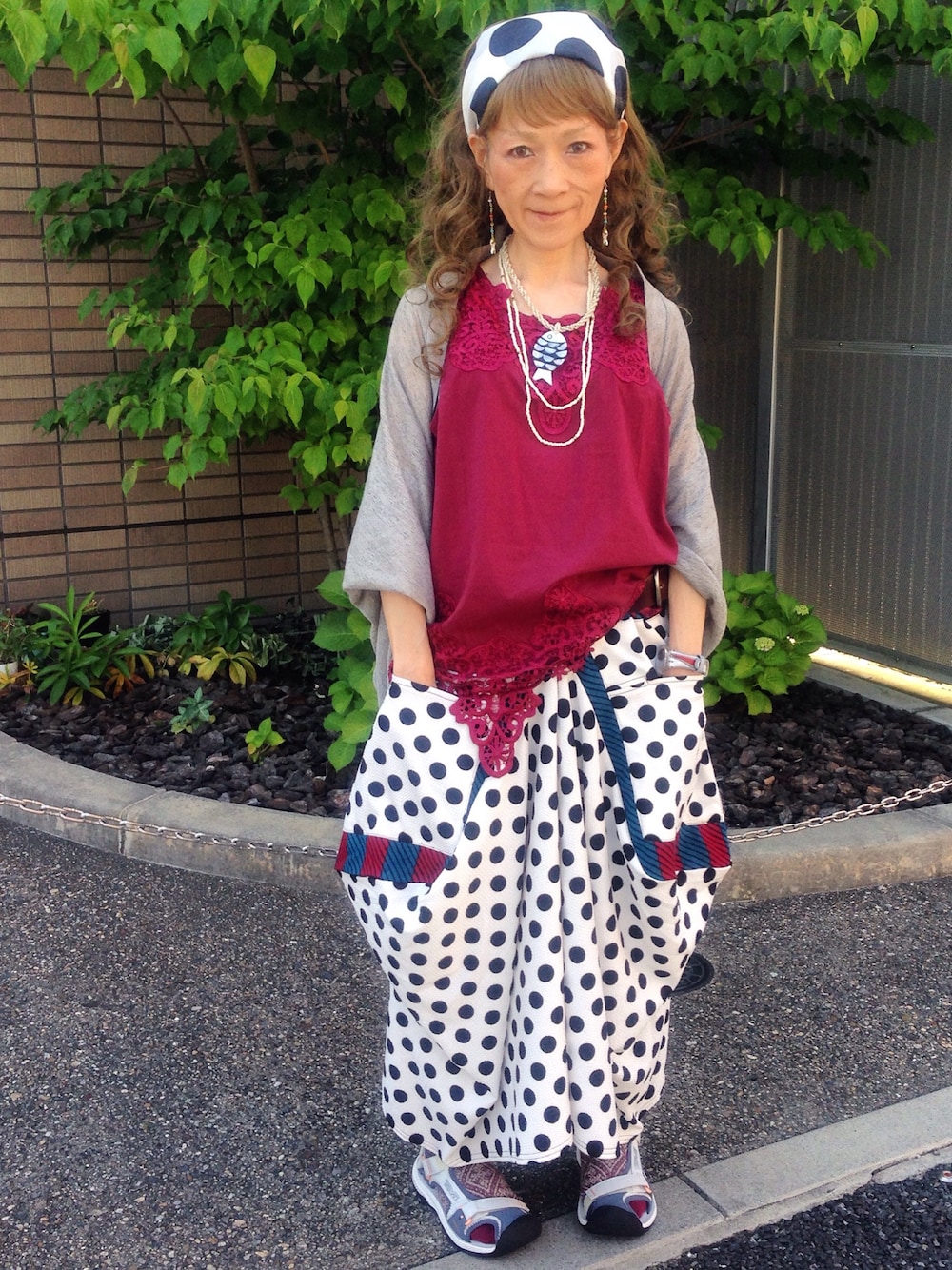 レッド系のタンクトップ、グレー系のカーディガン/ボレロ、ホワイト系のスカートを着用したレディースの春コーディネートの1枚目の写真