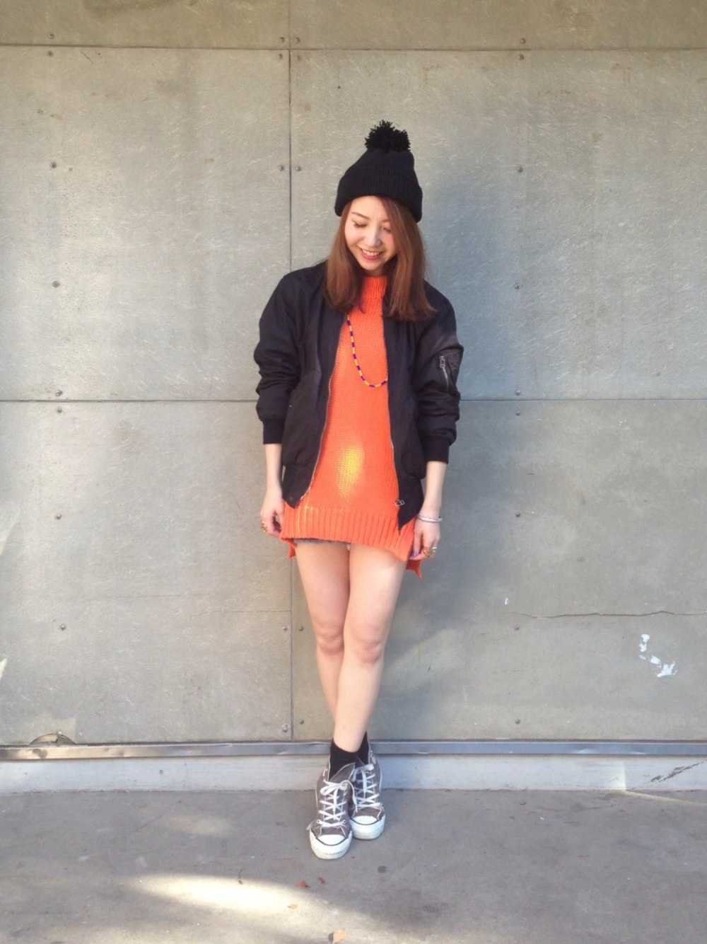 ブラック系のミリタリージャケット、オレンジ系のニット/セーター、グレー系のスニーカーを着用したレディースの冬コーディネートの1枚目の写真
