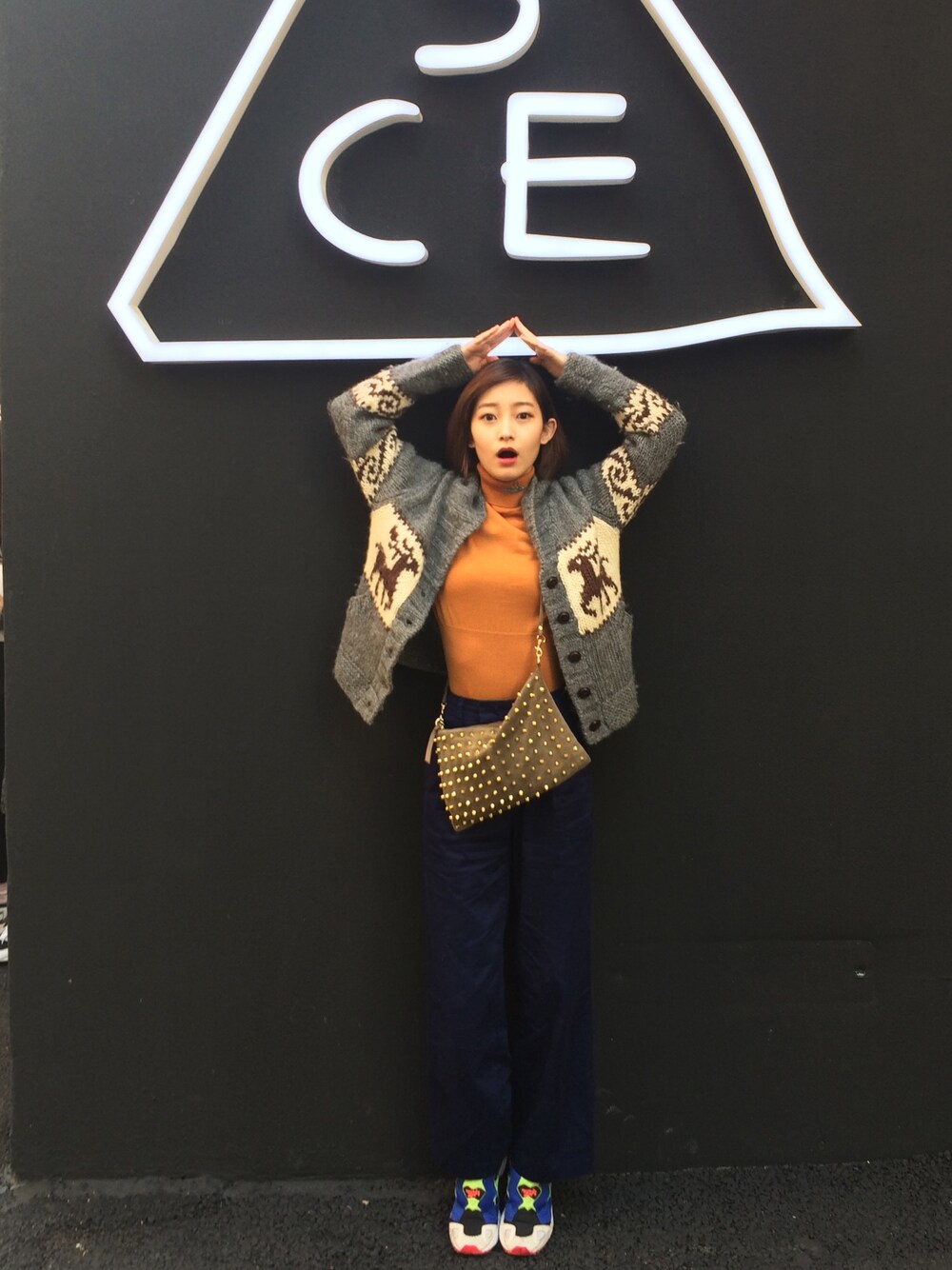 ゴールド系のニット/セーター、グリーン系のクラッチバッグ、ブルー系のパンツを着用したレディースの冬コーディネートの1枚目の写真