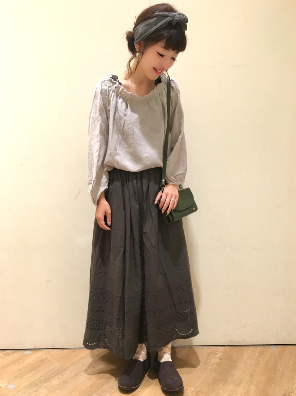 グレー系のトップス、グリーン系のショルダーバッグ、ブラウン系のブーツを着用したレディースの夏コーディネートの1枚目の写真