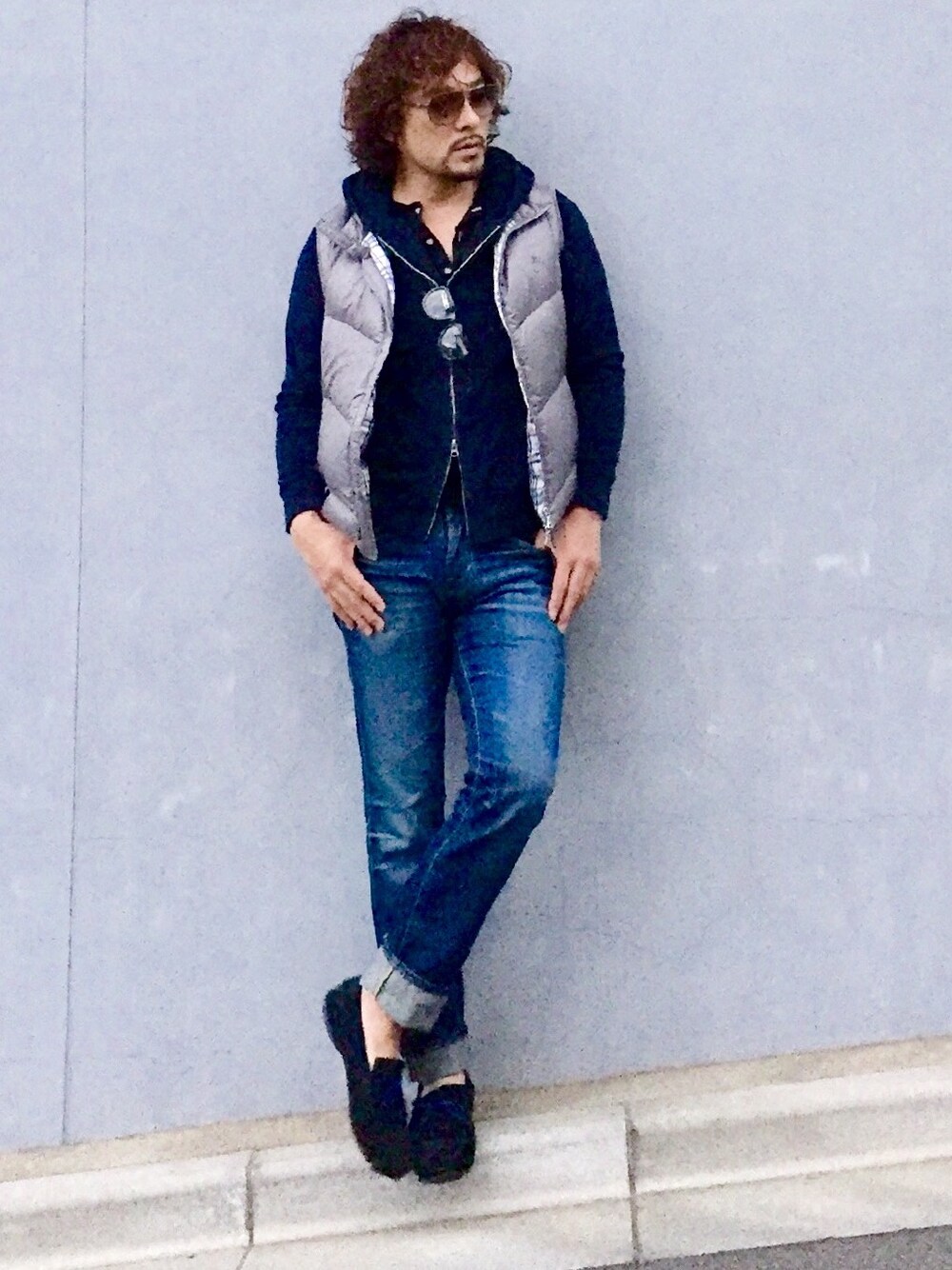 グレー系のダウンベスト、ブルー系のパーカー、ブルー系のデニムパンツを着用したメンズの秋コーディネートの1枚目の写真