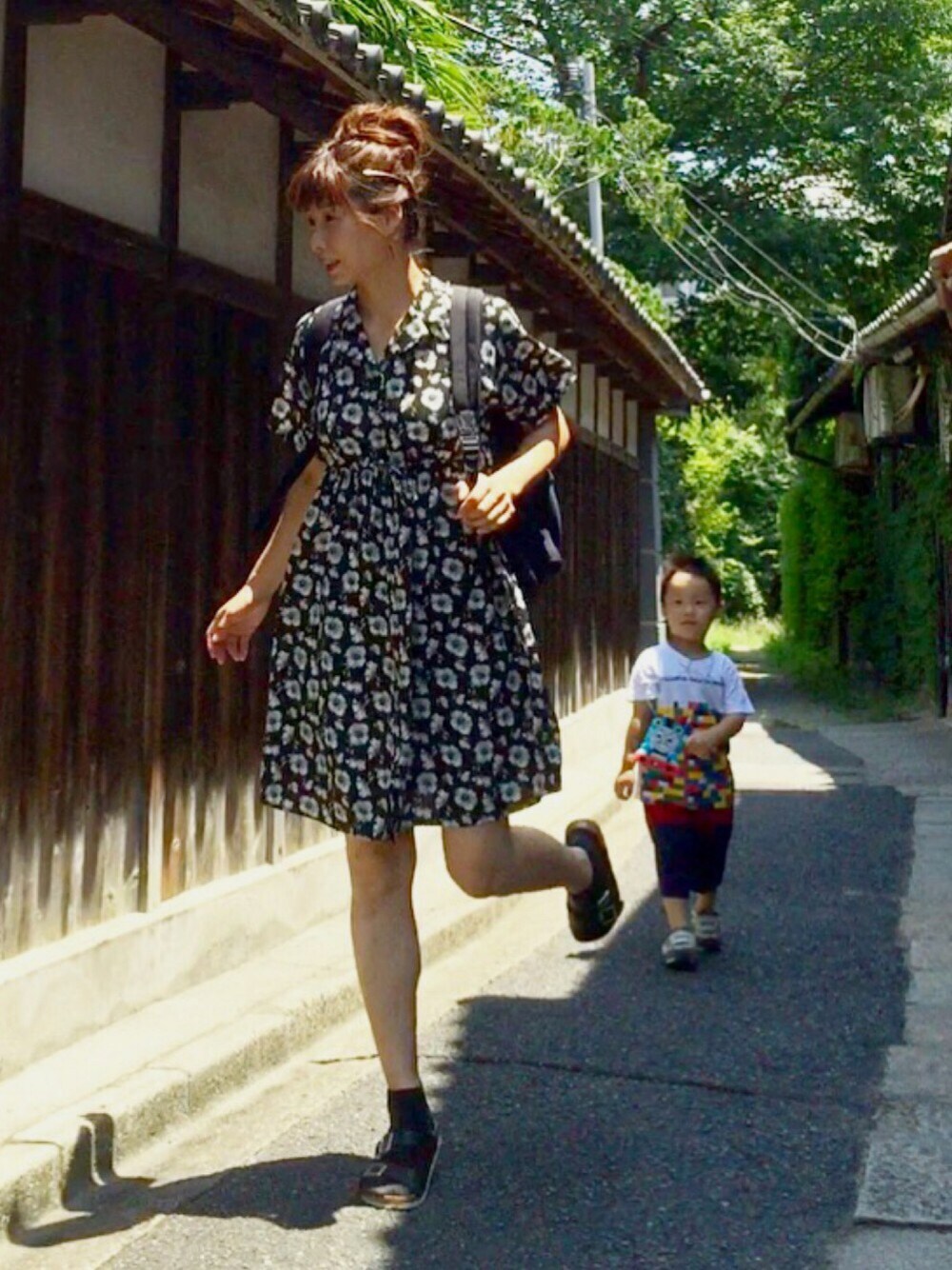 ブラック系のワンピース、ブラック系のサンダル、ブルー系のバックパック/リュックを着用したレディースの夏コーディネートの1枚目の写真