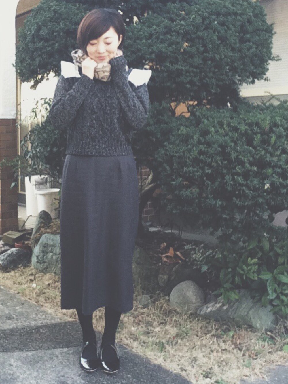 グレー系のニット/セーター、グレー系のスカート、ブラック系のパンプスを着用したレディースの冬コーディネートの1枚目の写真