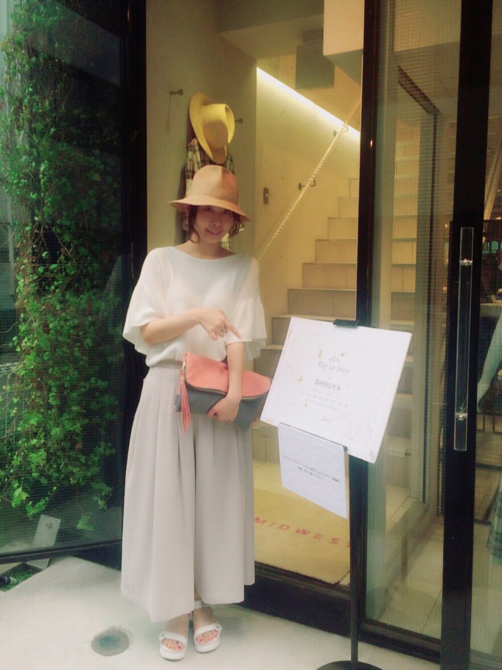グレー系のパンツ、ピンク系のクラッチバッグ、ホワイト系のサンダルを着用したレディースの夏コーディネートの1枚目の写真