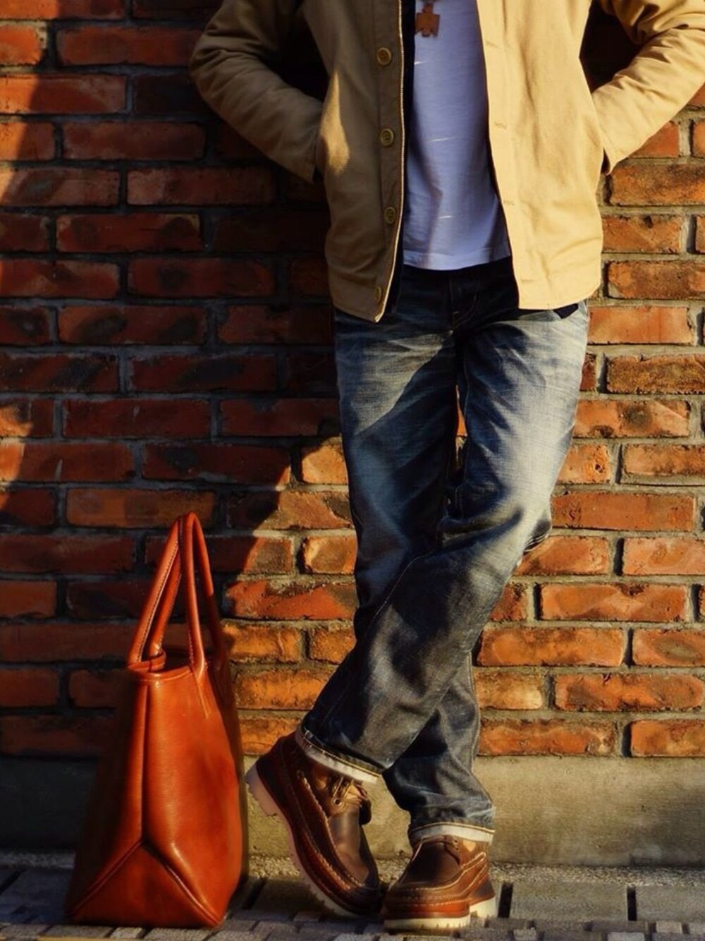 ブラウン系のトートバッグ、ホワイト系のTシャツ/カットソー、ベージュ系のピーコートを着用したメンズの夏コーディネートの1枚目の写真