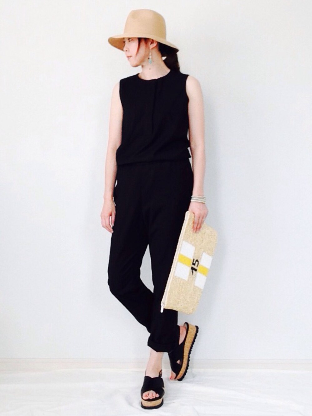 ブラック系のサロペット/オーバーオール、ベージュ系のクラッチバッグ、ブラック系のサンダルを着用したレディースの夏コーディネートの1枚目の写真