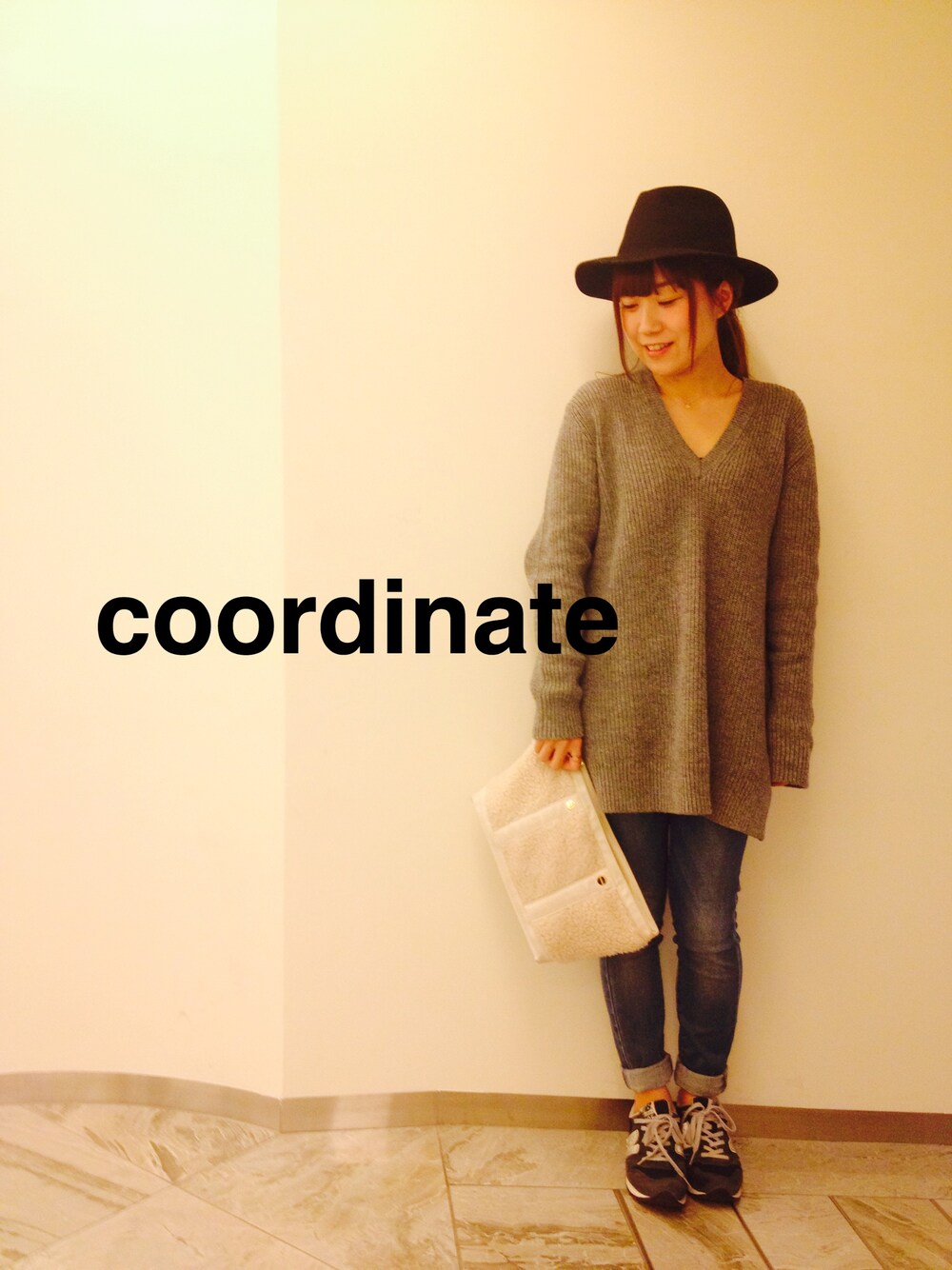 グレー系のニット/セーター、ホワイト系のクラッチバッグ、ブルー系のスニーカーを着用したレディースの冬コーディネートの1枚目の写真