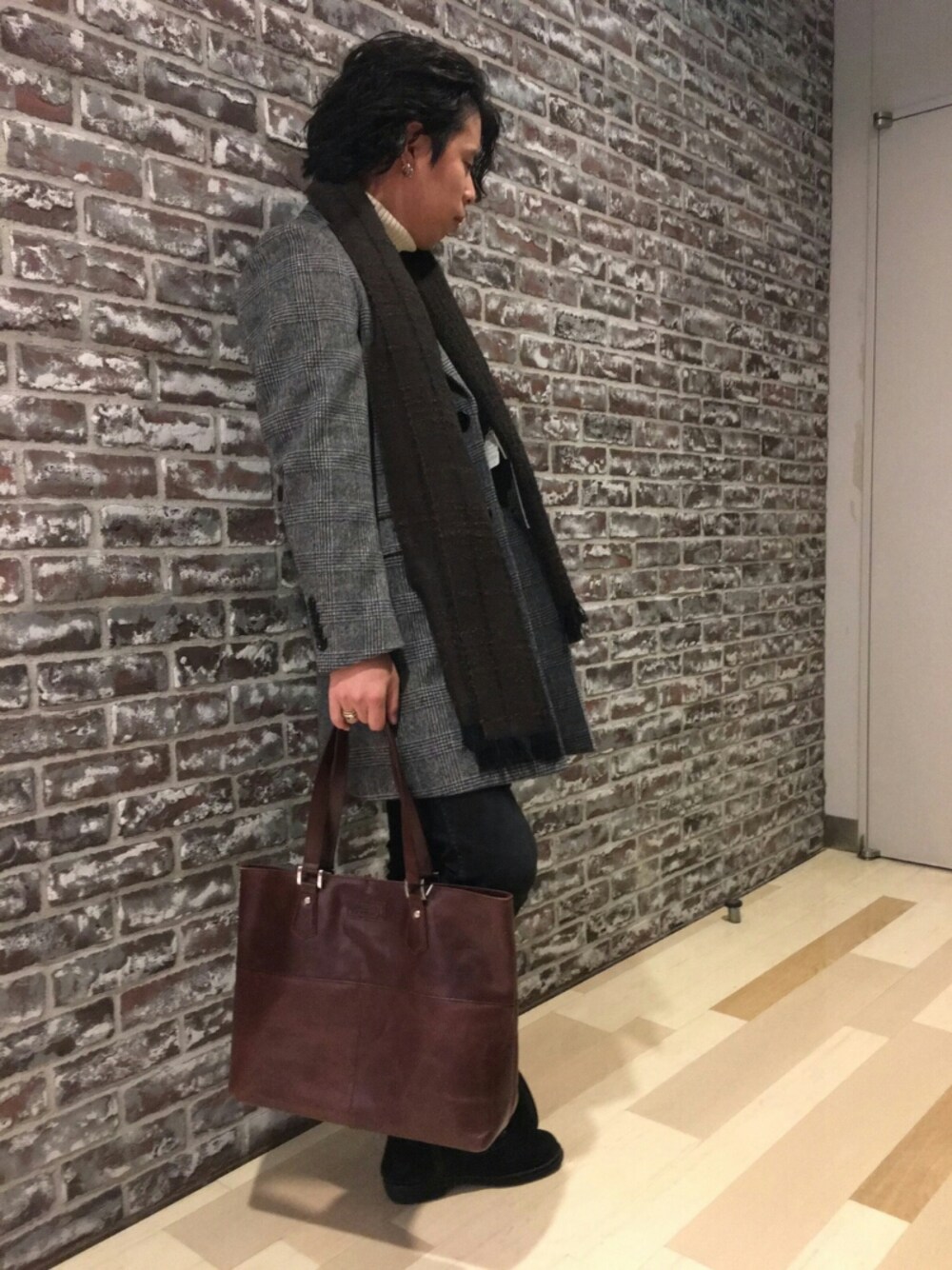 グレー系のチェスターコート、ブラウン系のトートバッグ、ホワイト系のニット/セーターを着用したメンズの秋コーディネートの1枚目の写真