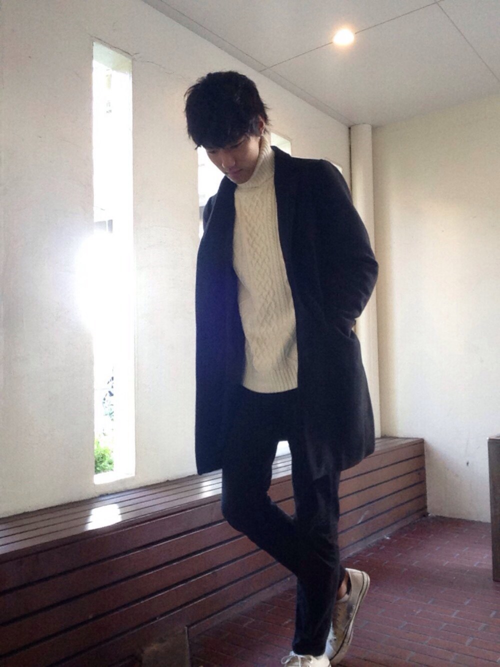 ベージュ系のスニーカー、ホワイト系のニット/セーター、ブラック系のチェスターコートを着用したメンズの秋コーディネートの1枚目の写真