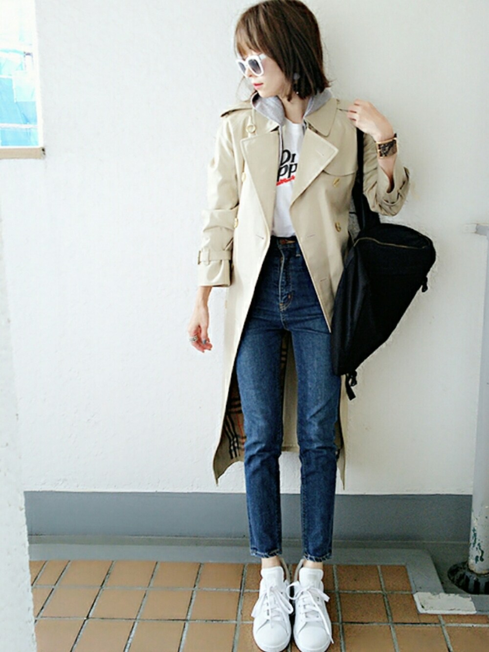 ベージュ系のトレンチコート、ホワイト系のTシャツ/カットソー、ブルー系のデニムパンツを着用したレディースの秋コーディネートの1枚目の写真