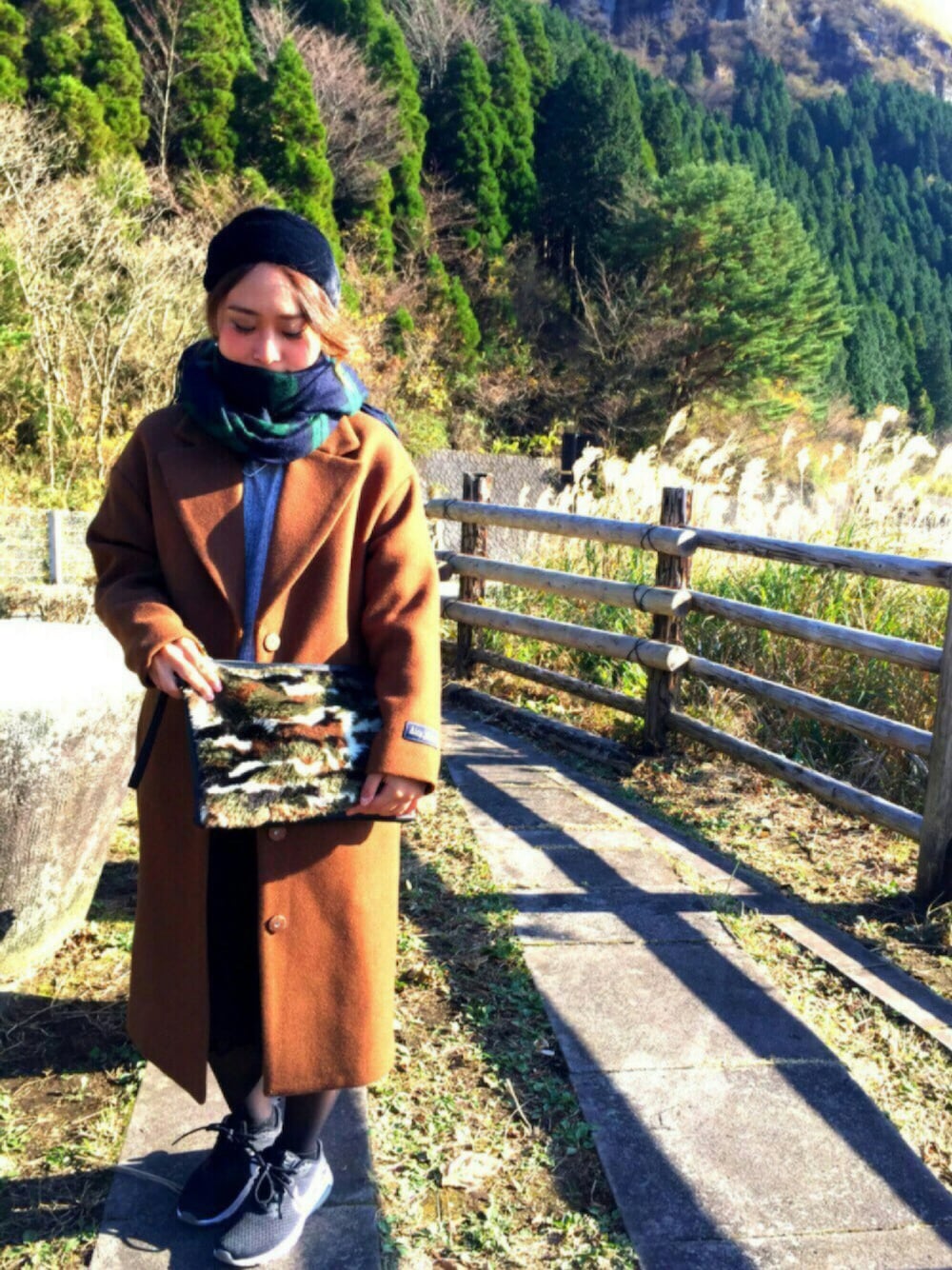 ブラウン系のチェスターコート、グレー系のニット/セーター、ブラック系のスカートを着用したレディースの冬コーディネートの1枚目の写真