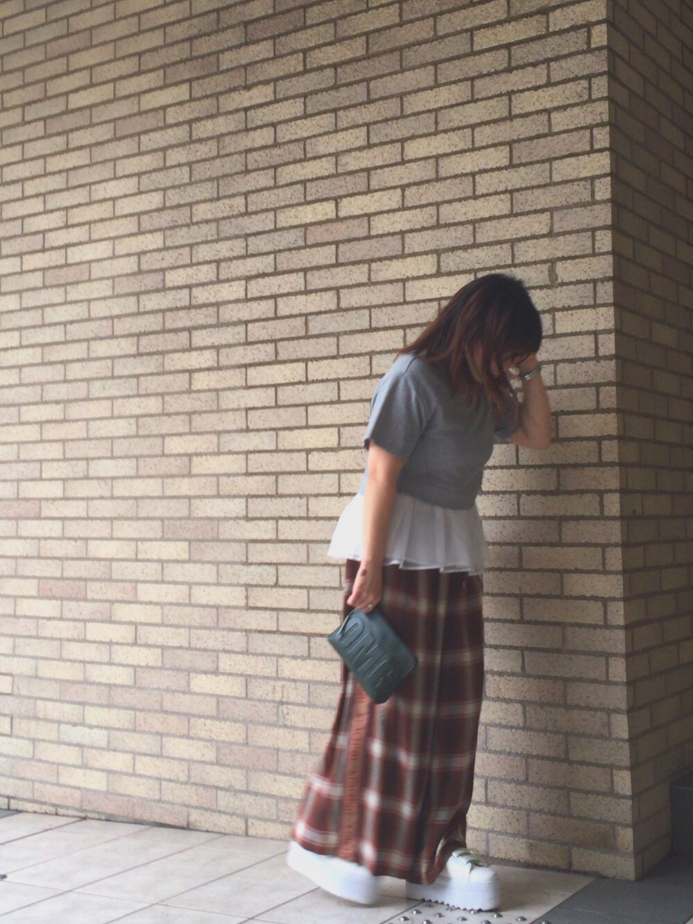 ブラウン系のパンツ、グリーン系のクラッチバッグ、グレー系のトップスを着用したレディースの秋コーディネートの1枚目の写真