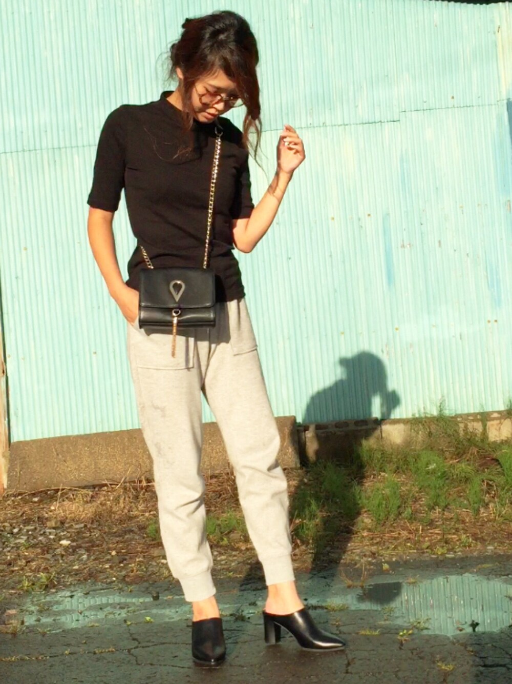 ブラック系のトップス、グレー系のパンツ、ブラック系のショルダーバッグを着用したレディースの夏コーディネートの1枚目の写真