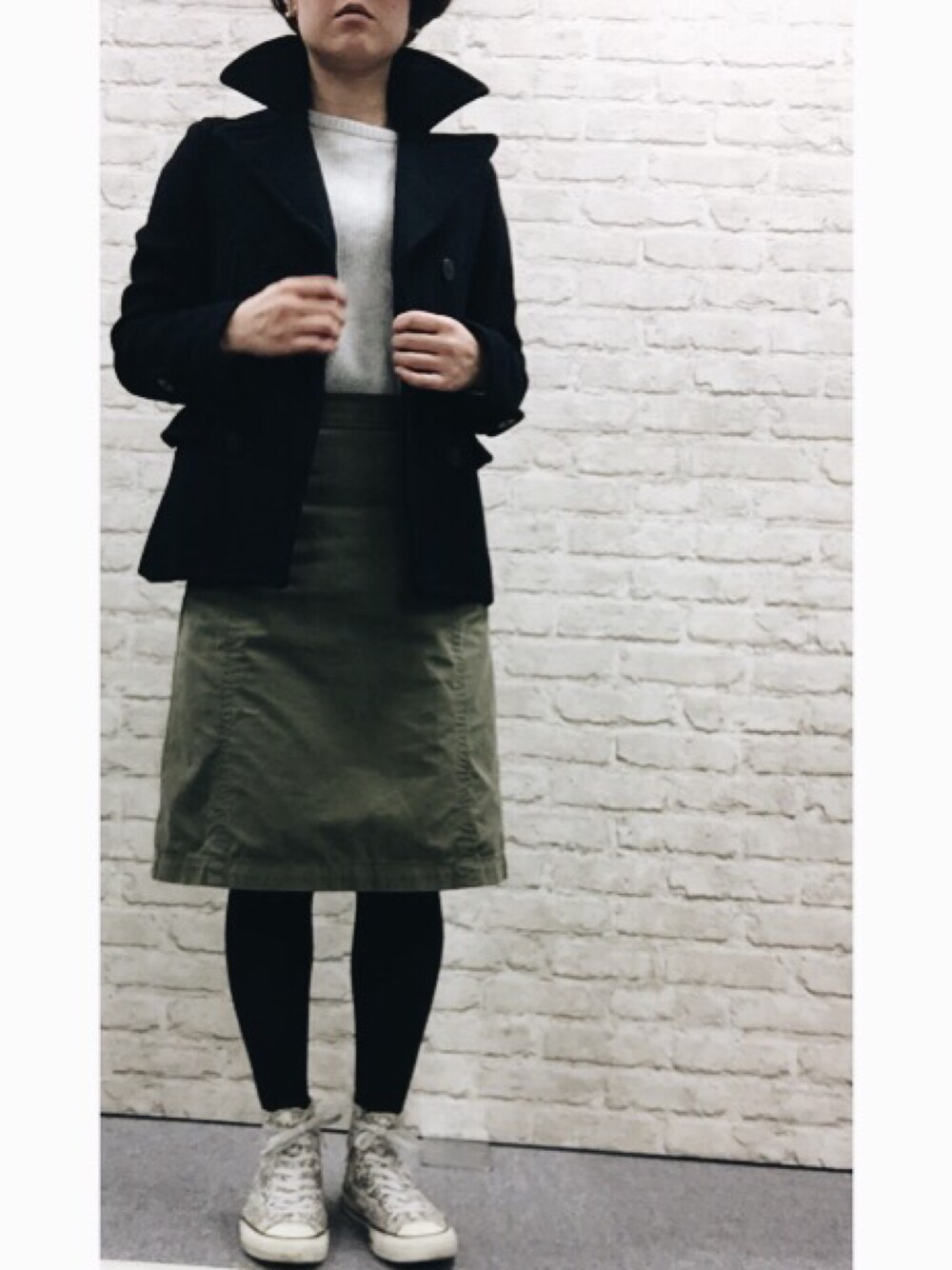 ブラック系のピーコート、グレー系のニット/セーター、グリーン系のスカートを着用したレディースの冬コーディネートの1枚目の写真