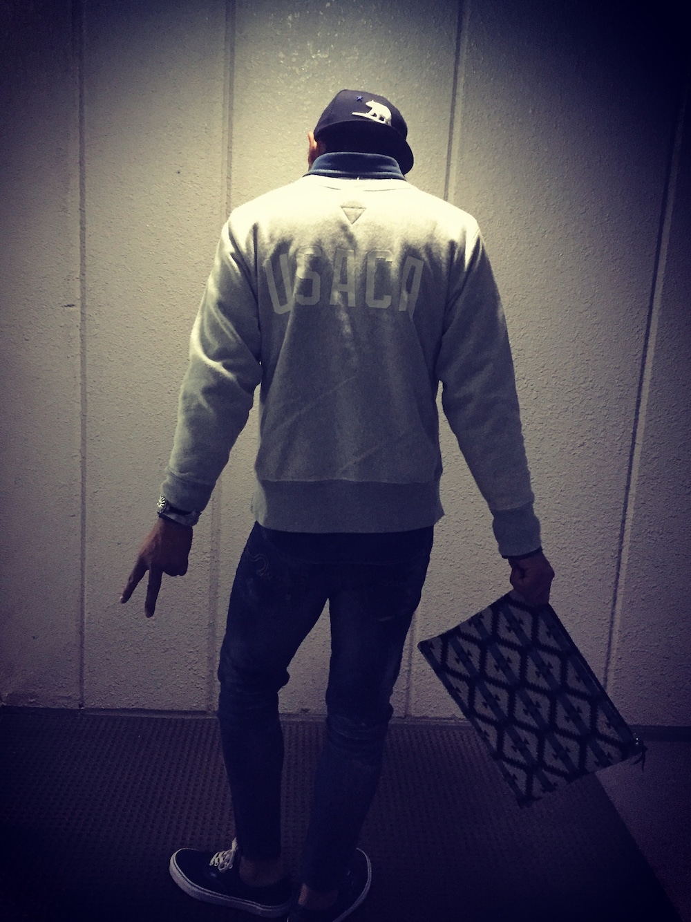 グレー系のスウェット、ブルー系のデニムパンツ、ホワイト系のクラッチバッグを着用したメンズの春コーディネートの1枚目の写真