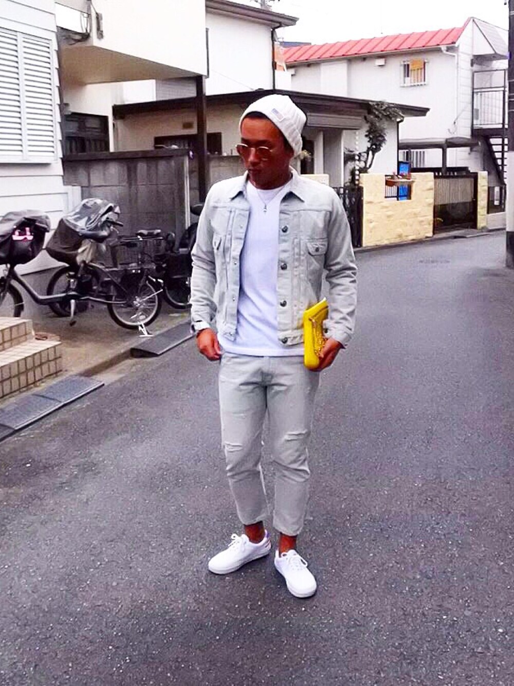 イエロー系のクラッチバッグ、ホワイト系のシューズ、グレー系のデニムジャケットを着用したメンズの秋コーディネートの1枚目の写真