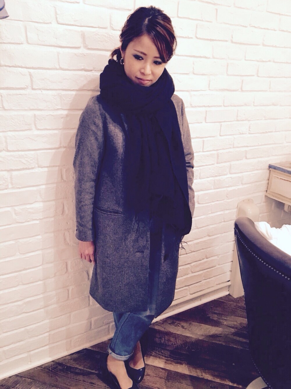 グレー系のチェスターコート、ブルー系のデニムパンツ、ブラック系のストール/ショールを着用したレディースの冬コーディネートの1枚目の写真