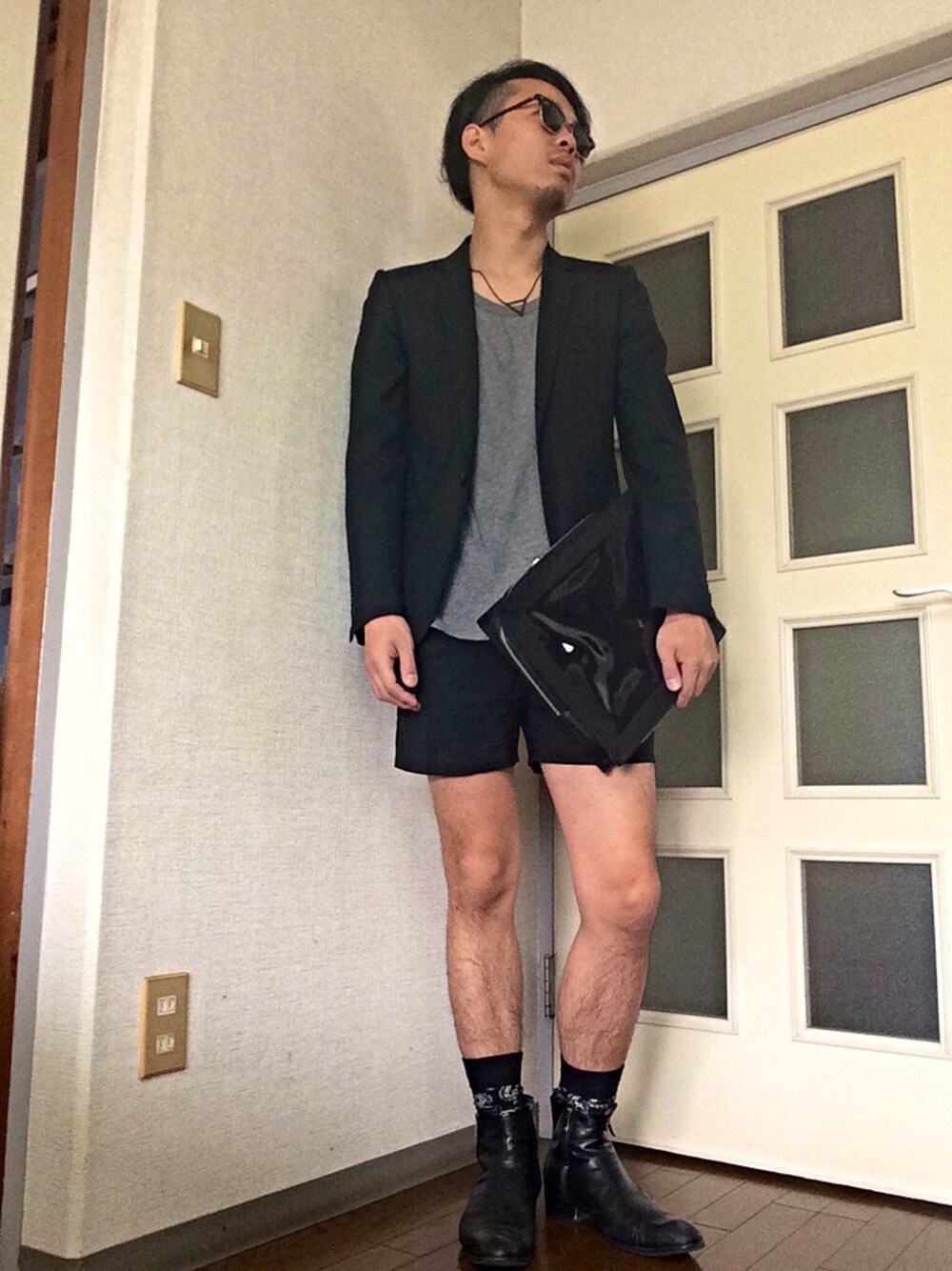 ブルー系のクラッチバッグ、ブラック系のテーラードジャケット、ブラック系のネックレスを着用したメンズの春コーディネートの1枚目の写真