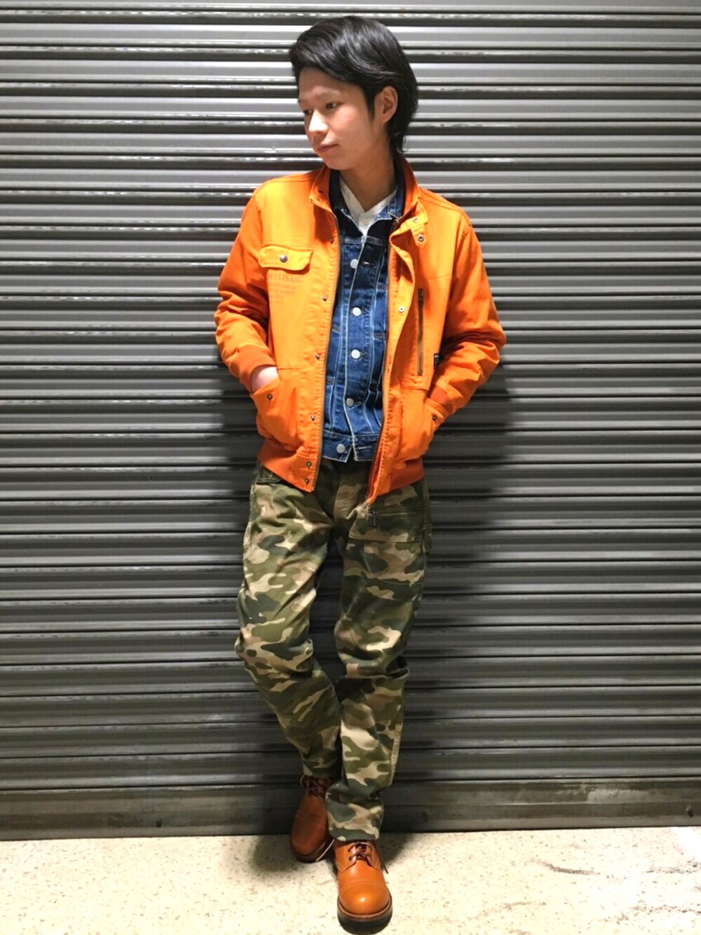 オレンジ系のミリタリージャケット、ブルー系のブルゾン、オレンジ系のブーツを着用したメンズの春コーディネートの1枚目の写真