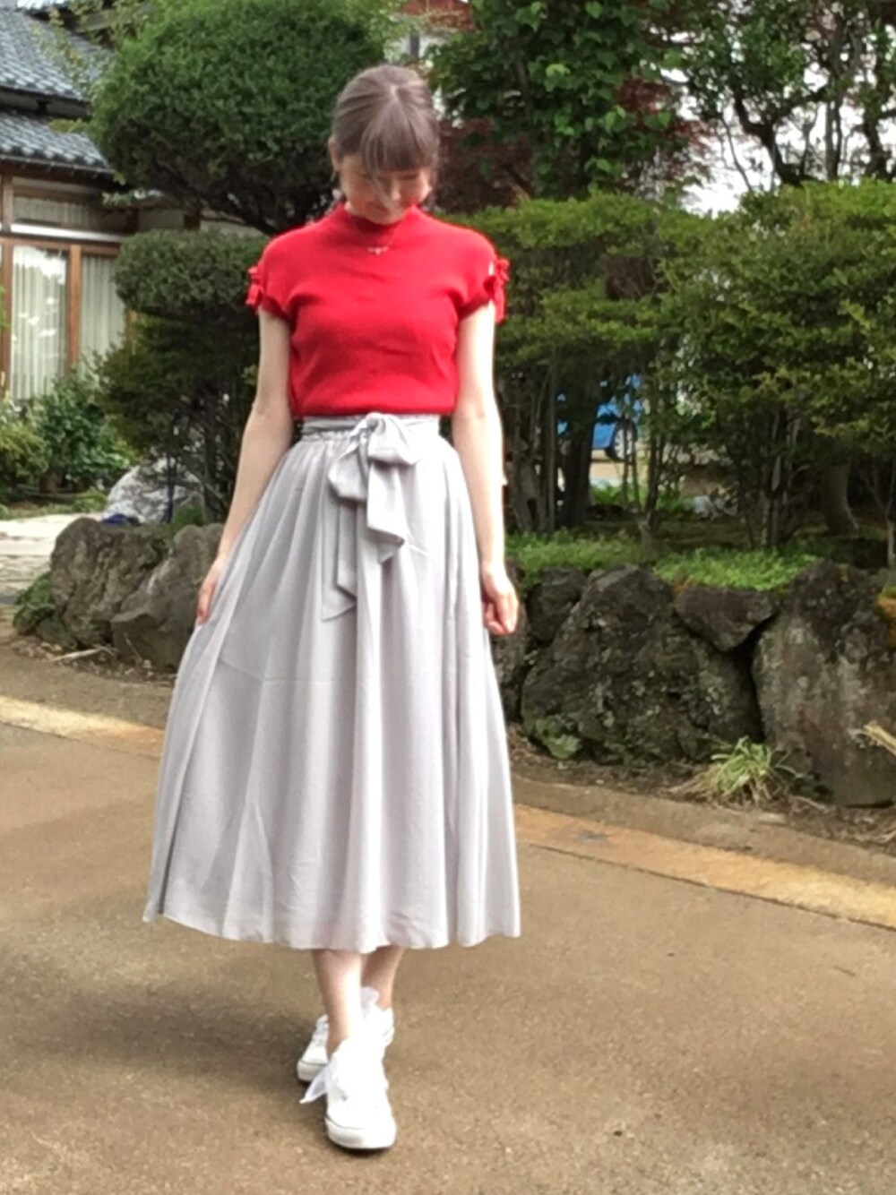 レッド系のニット/セーター、グレー系のスカート、ホワイト系のスニーカーを着用したレディースの夏コーディネートの1枚目の写真