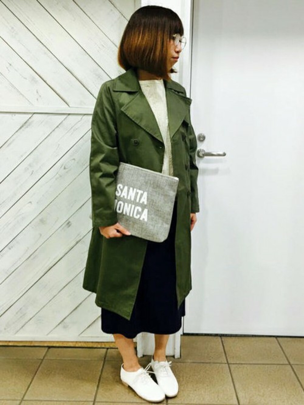 グリーン系のトレンチコート、グレー系のクラッチバッグ、ホワイト系のその他シューズを着用したレディースの春コーディネートの1枚目の写真