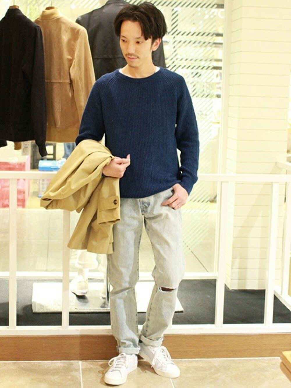 ブルー系のニット/セーター、ベージュ系のステンカラーコート、ブラック系のスニーカーを着用したメンズの冬コーディネートの1枚目の写真