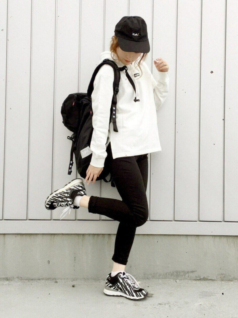 ホワイト系のパーカー、ブラック系のバックパック/リュック、ブラック系のスニーカーを着用したレディースの秋コーディネートの1枚目の写真