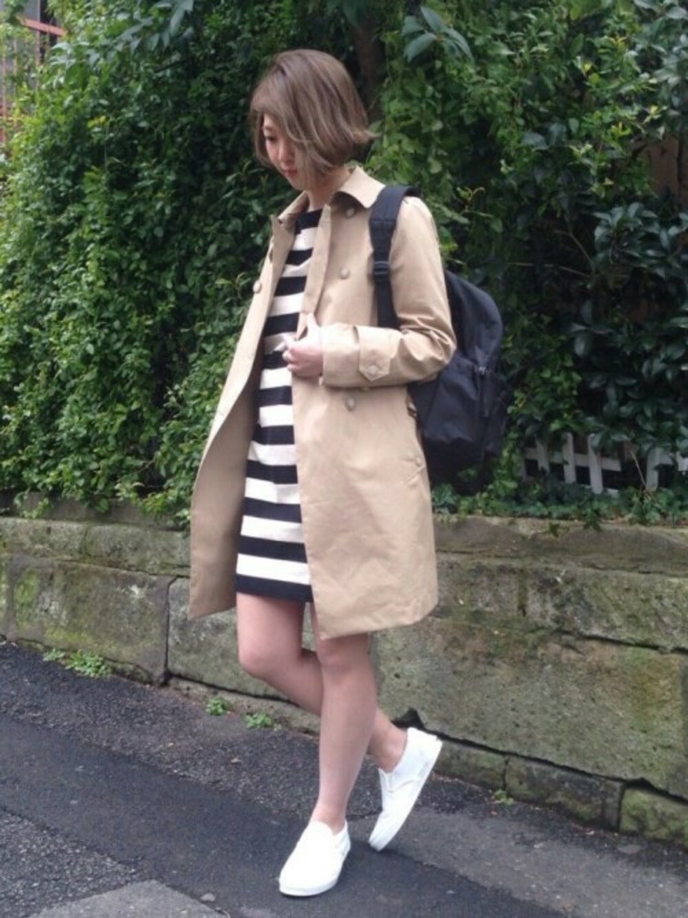 ベージュ系のトレンチコート、ブラック系のワンピース、ブラック系のバックパック/リュックを着用したレディースの冬コーディネートの1枚目の写真