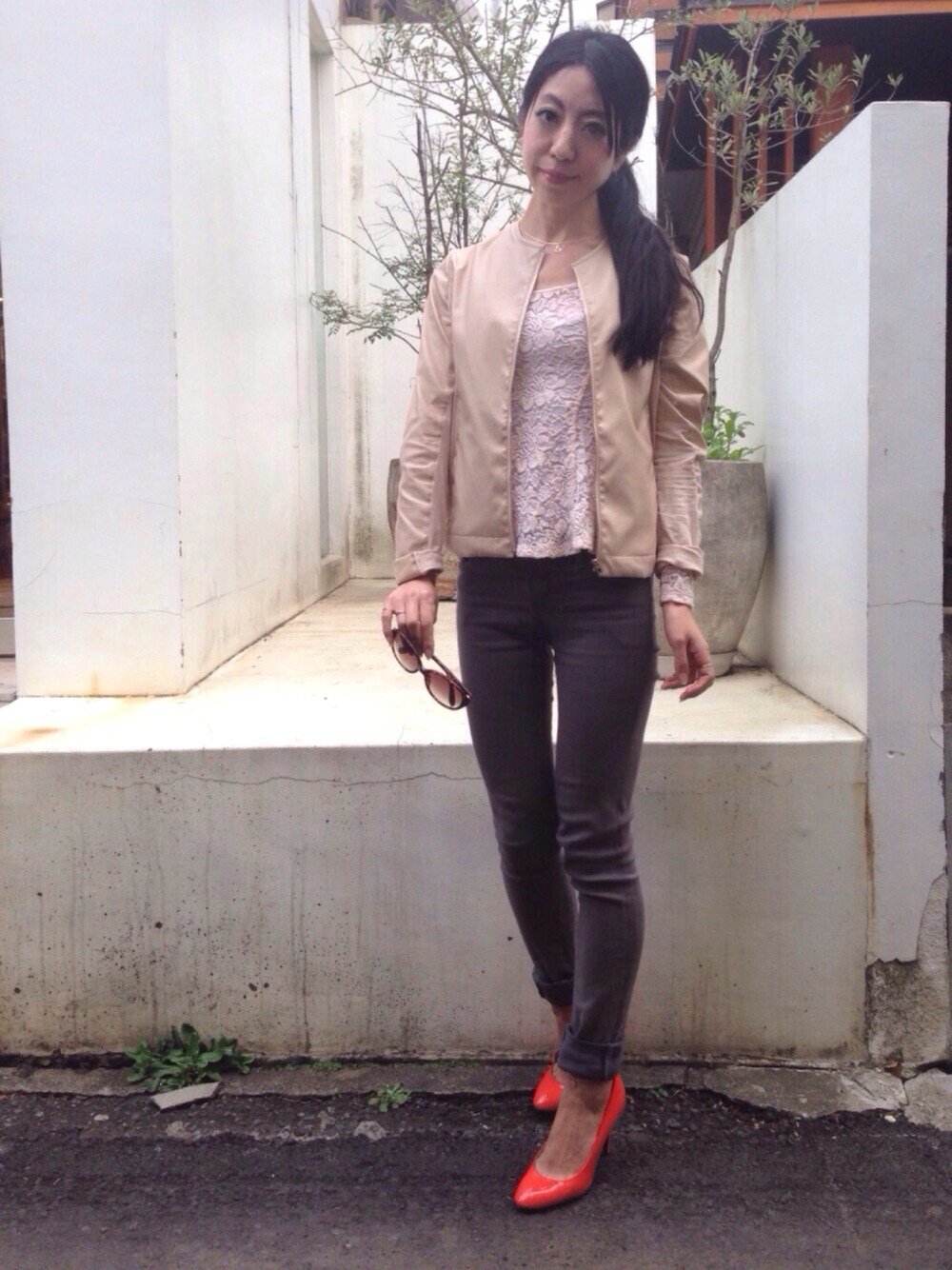 グレー系のデニムパンツ、オレンジ系のパンプス、ベージュ系のノーカラージャケットを着用したレディースの春コーディネートの1枚目の写真