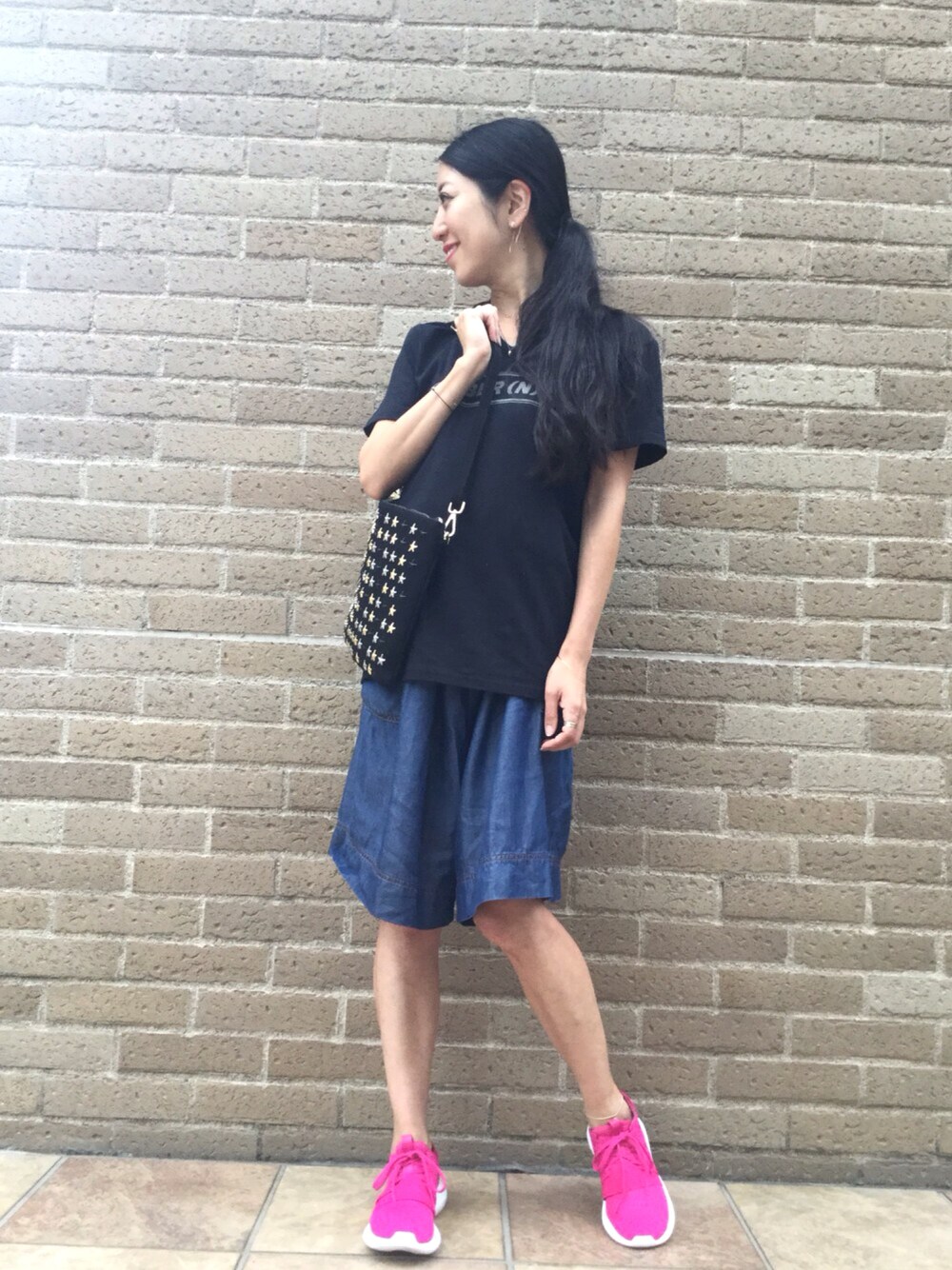 ブラック系のクラッチバッグ、ピンク系のスニーカー、ブラック系のTシャツ/カットソーを着用したレディースの夏コーディネートの1枚目の写真