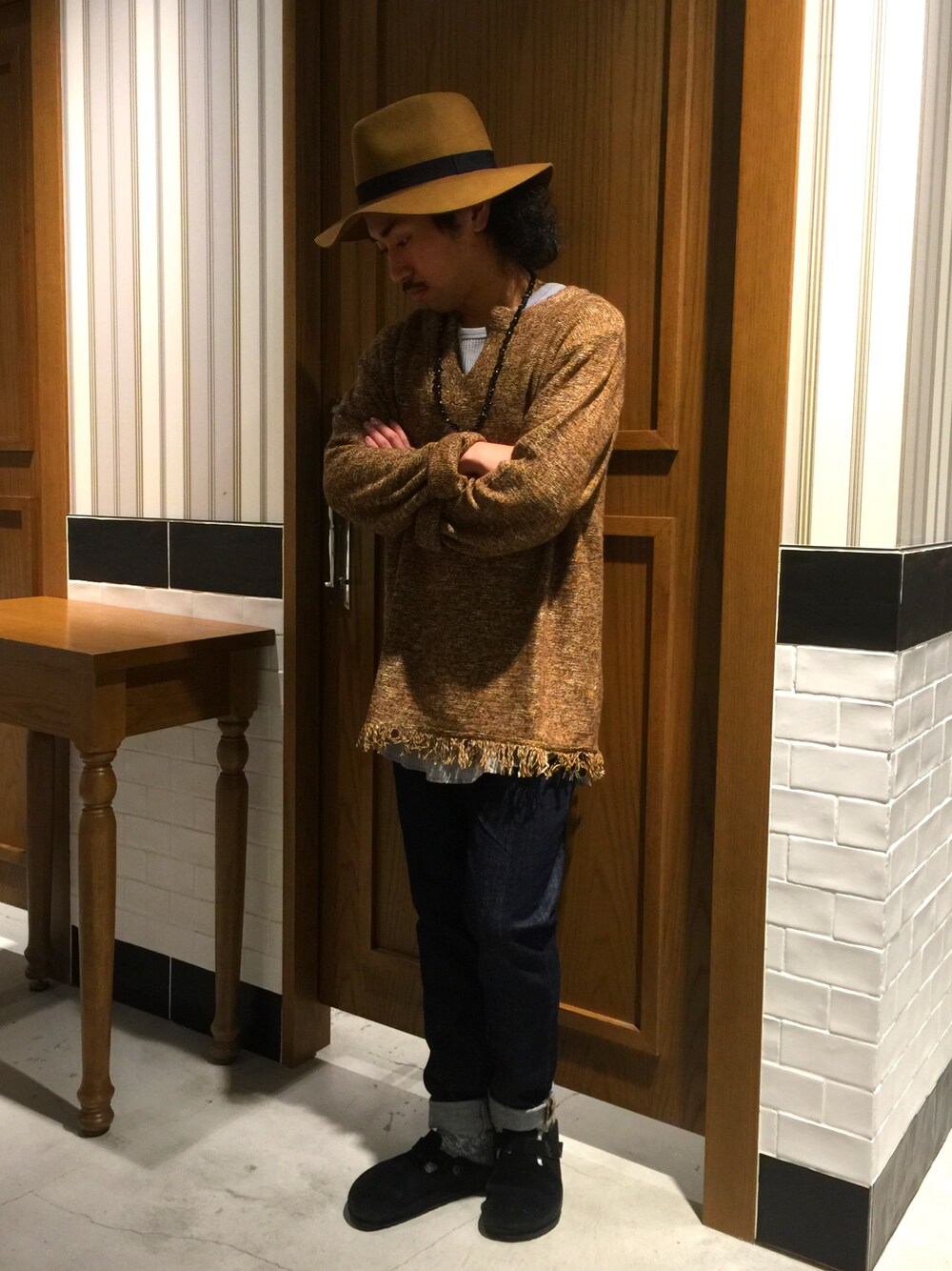 ブラウン系のニット/セーター、グレー系のTシャツ/カットソー、ブルー系のデニムパンツを着用したメンズの秋コーディネートの1枚目の写真