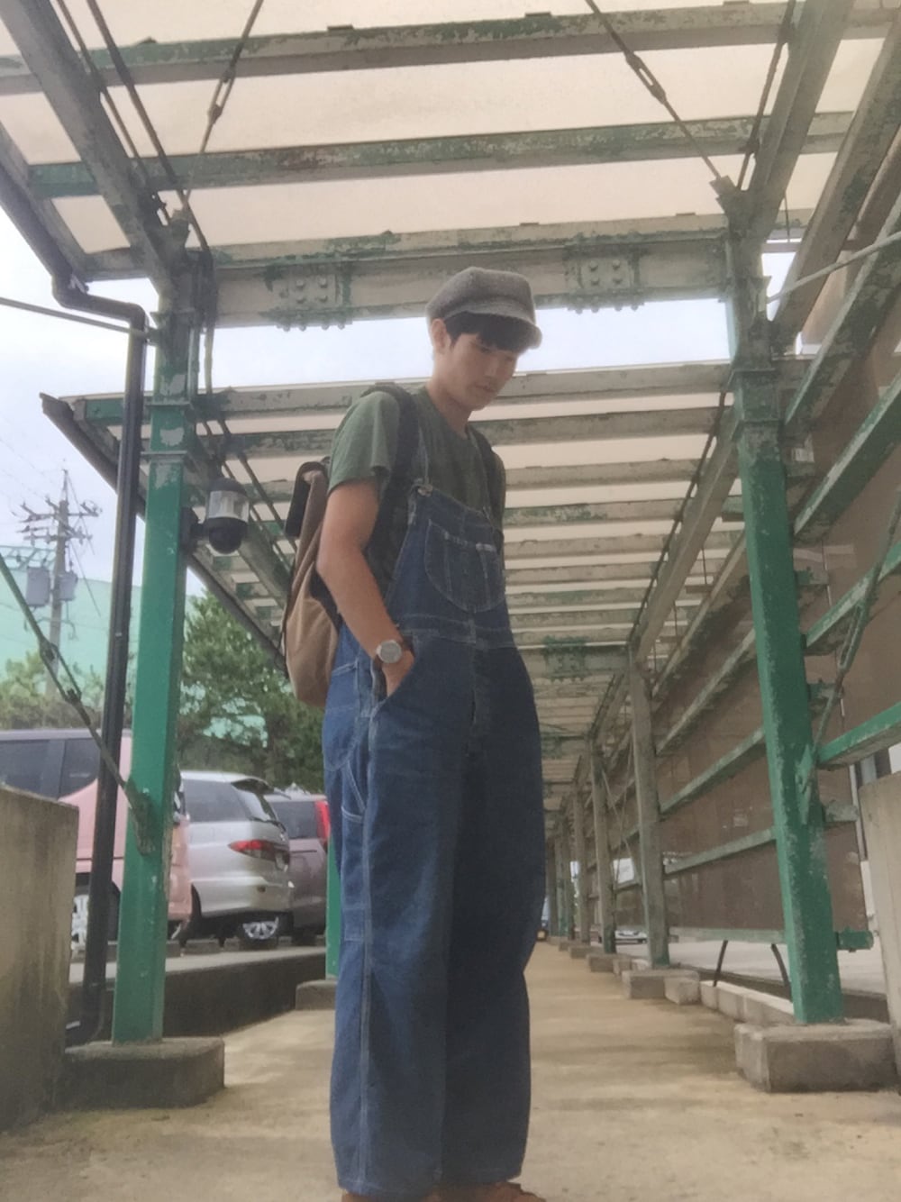 グリーン系のTシャツ/カットソー、ブルー系のサロペット/オーバーオール、ベージュ系のバックパック/リュックを着用したメンズの夏コーディネートの1枚目の写真
