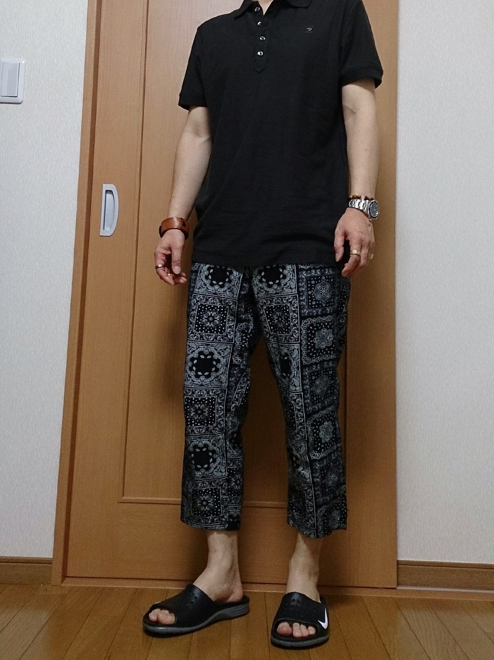 ブラック系のポロシャツ、ブラック系のパンツ、ブラック系のサンダルを着用したメンズの夏コーディネートの1枚目の写真