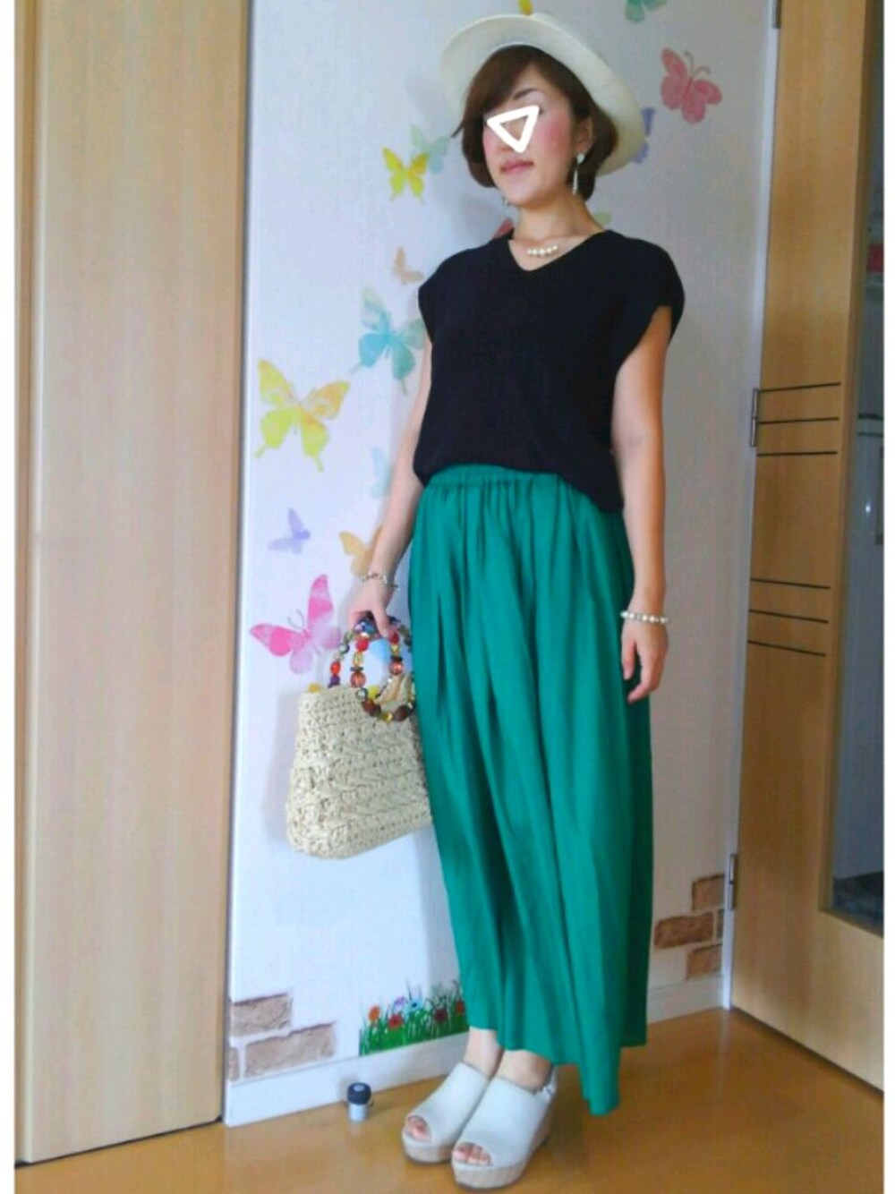 ベージュ系のかごバッグ、グリーン系のスカート、ブラック系のニット/セーターを着用したレディースの夏コーディネートの1枚目の写真